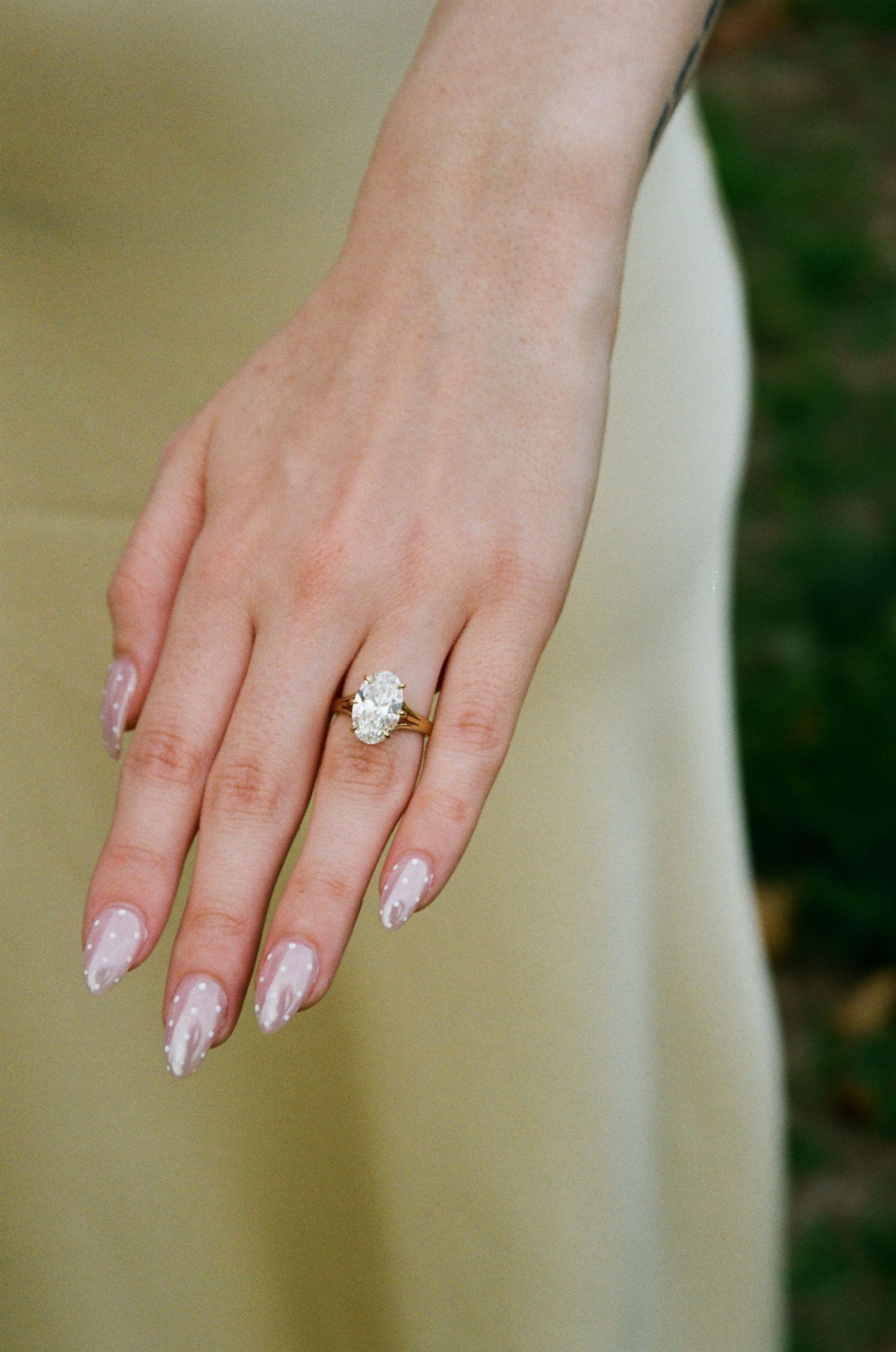 Close-up of an oval diamond engagement ring on a gold band on a woman's hand with glitter nails.