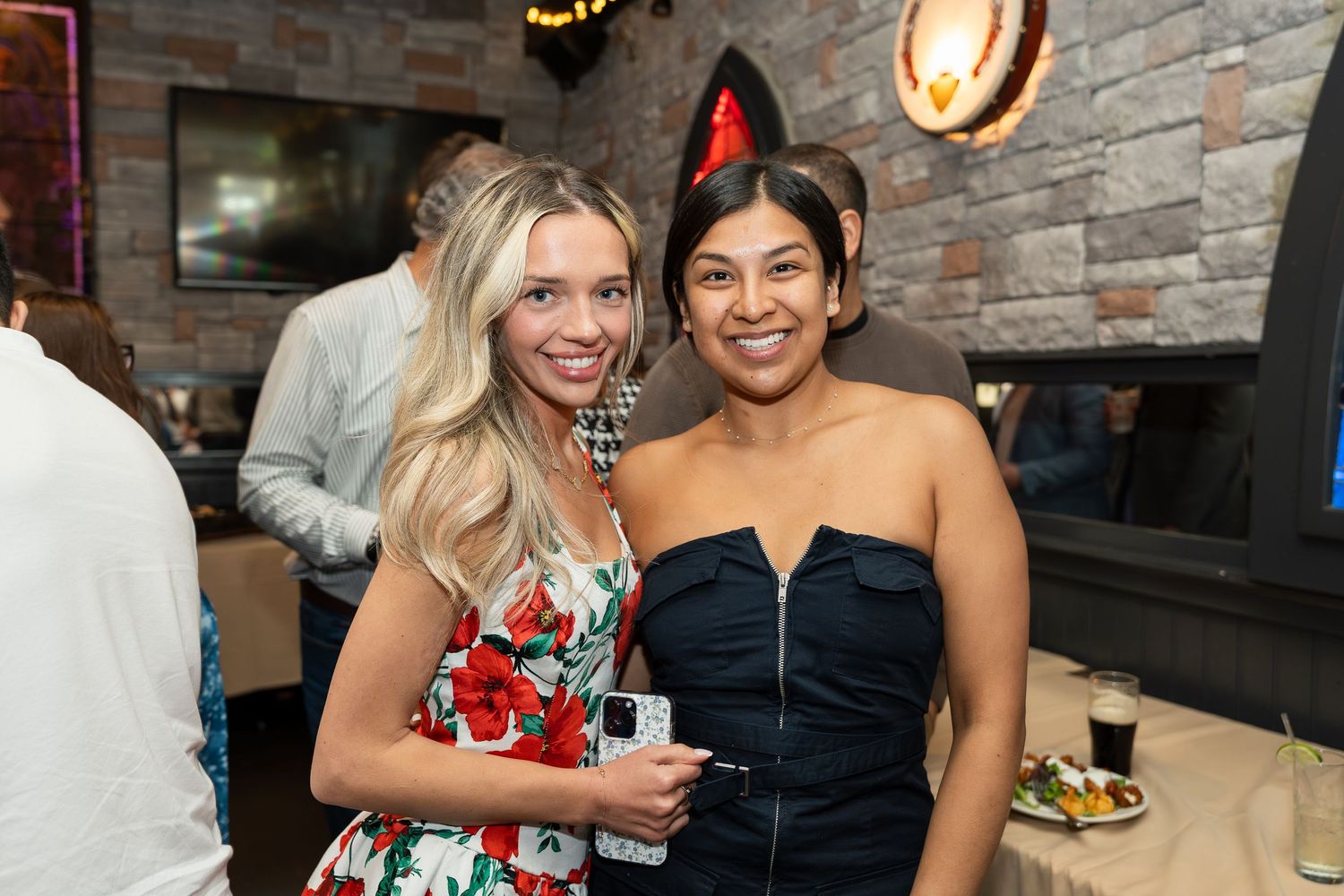 Two young women smiling together at a festive indoor party event.