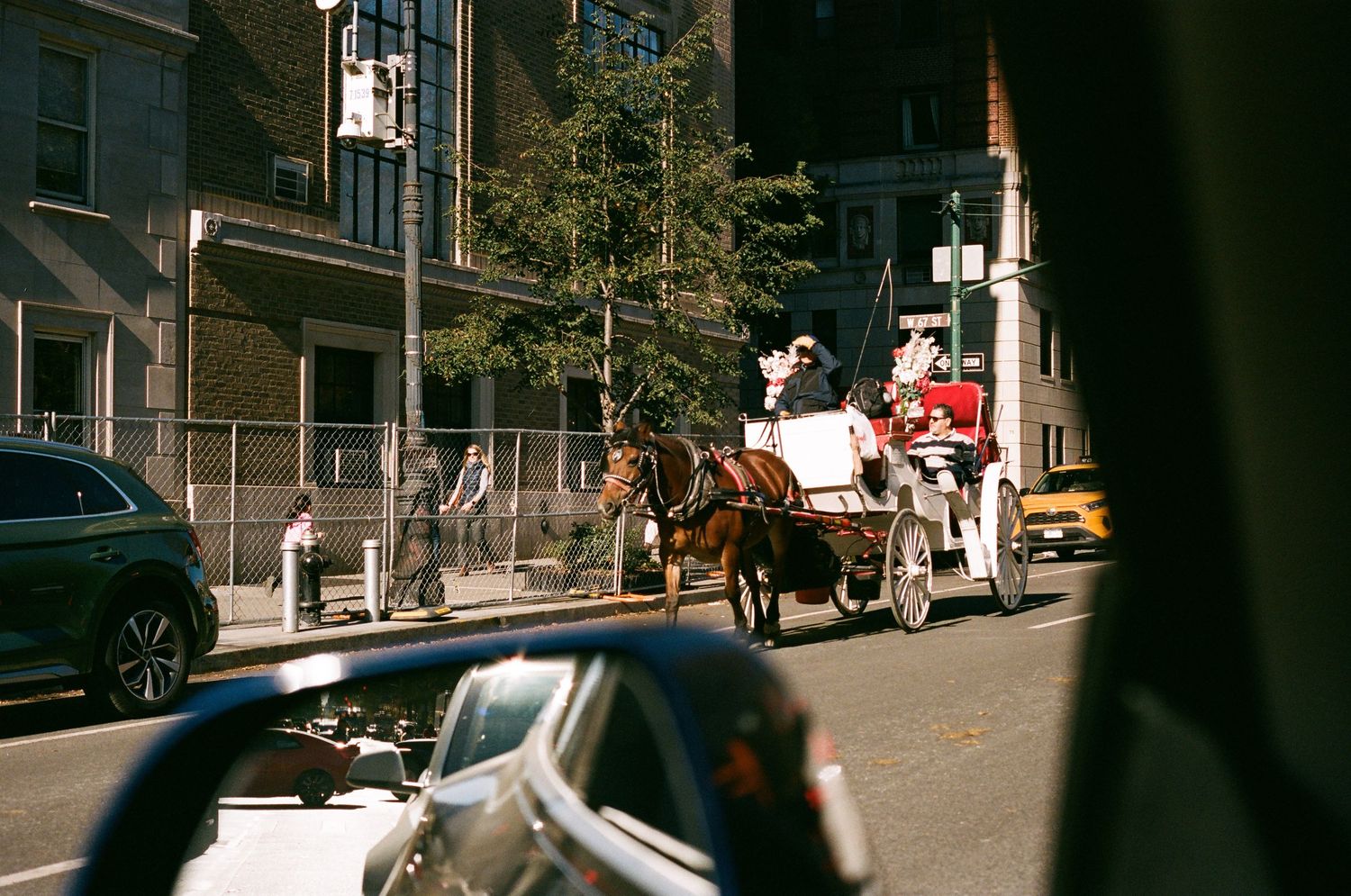 A horse-drawn white carriage rides through a busy New York City street alongside modern cars.