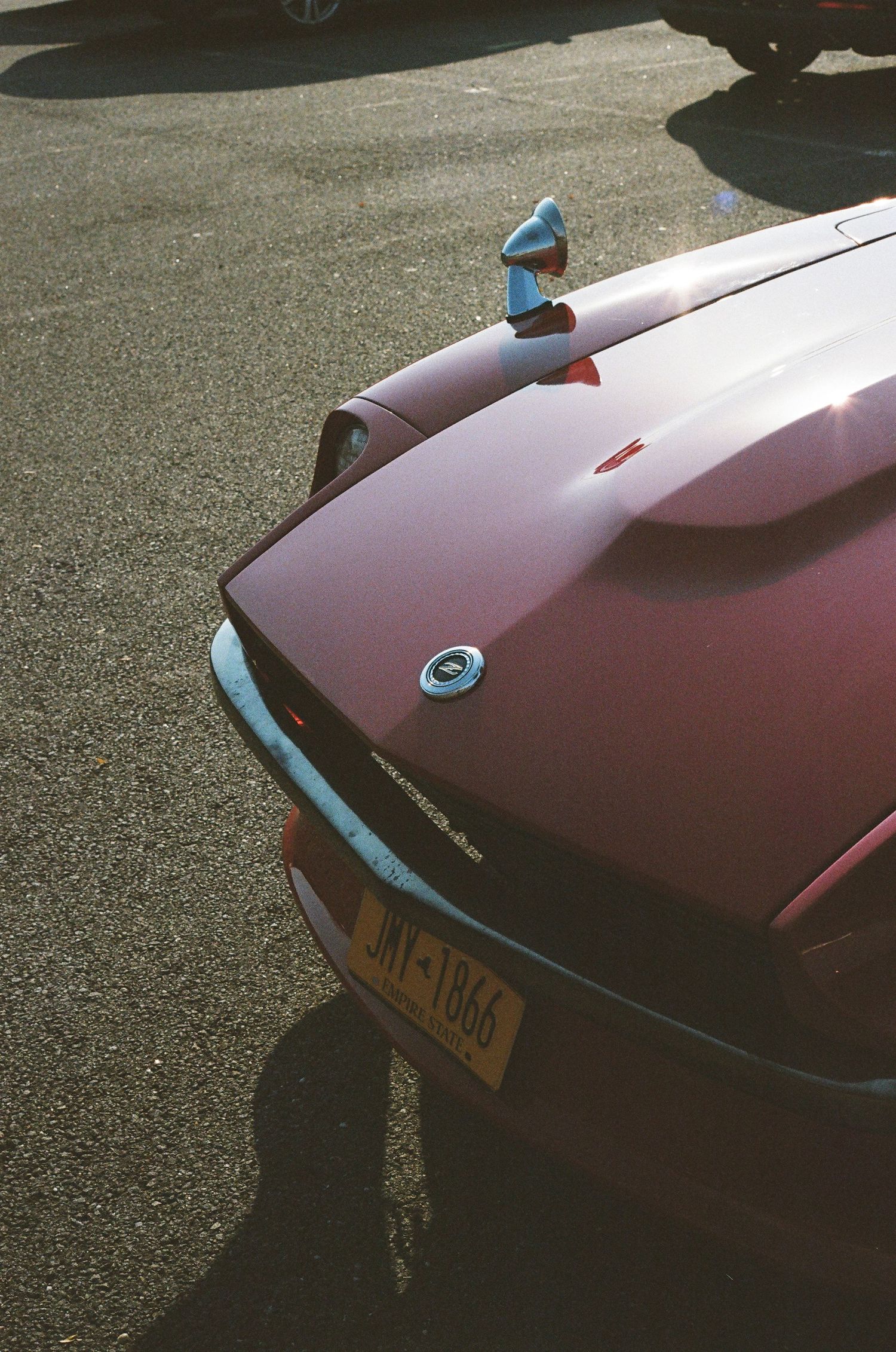 Rear view of vintage red sports car with yellow license plate JAY-1866 in parking lot.