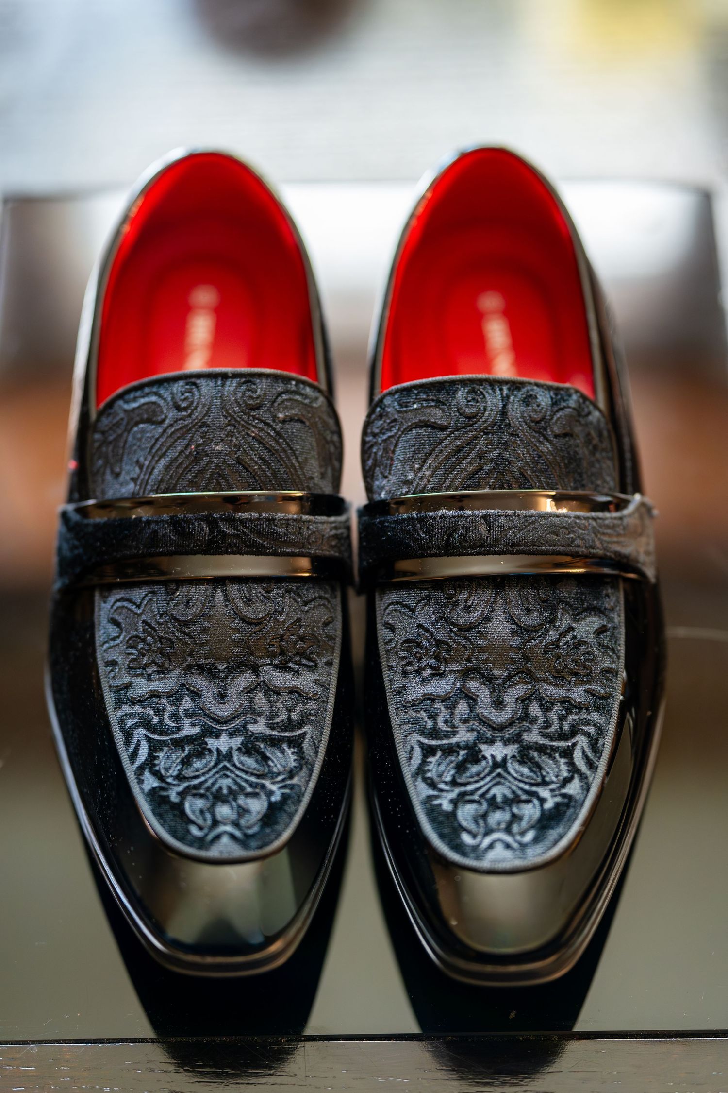 Elegant pair of black paisley embroidered loafers with red interior lining displayed on a reflective surface.