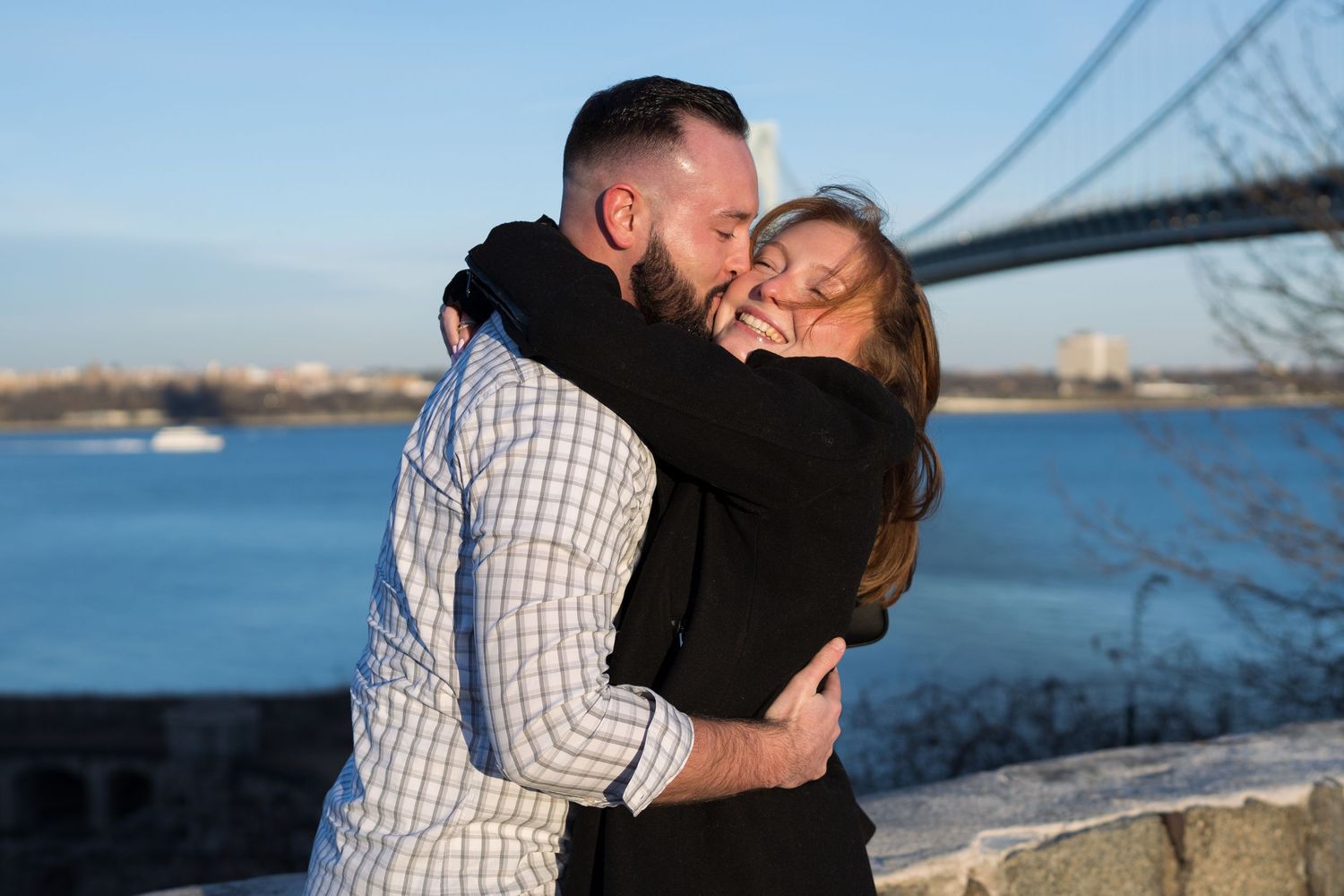 Happy couple hugging and smiling together with the Verrazzano-Narrows Bridge in the background.