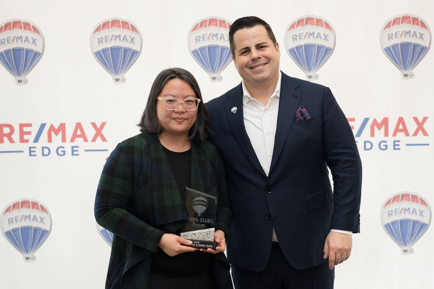 Woman and man pose together holding a crystal award at a RE/MAX Edge real estate event.