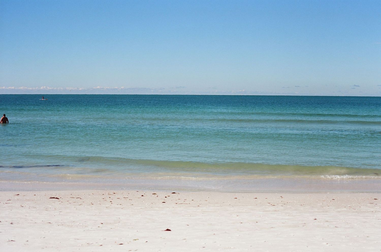 Pristine white sandy beach with calm turquoise waters and clear blue sky on a sunny day.