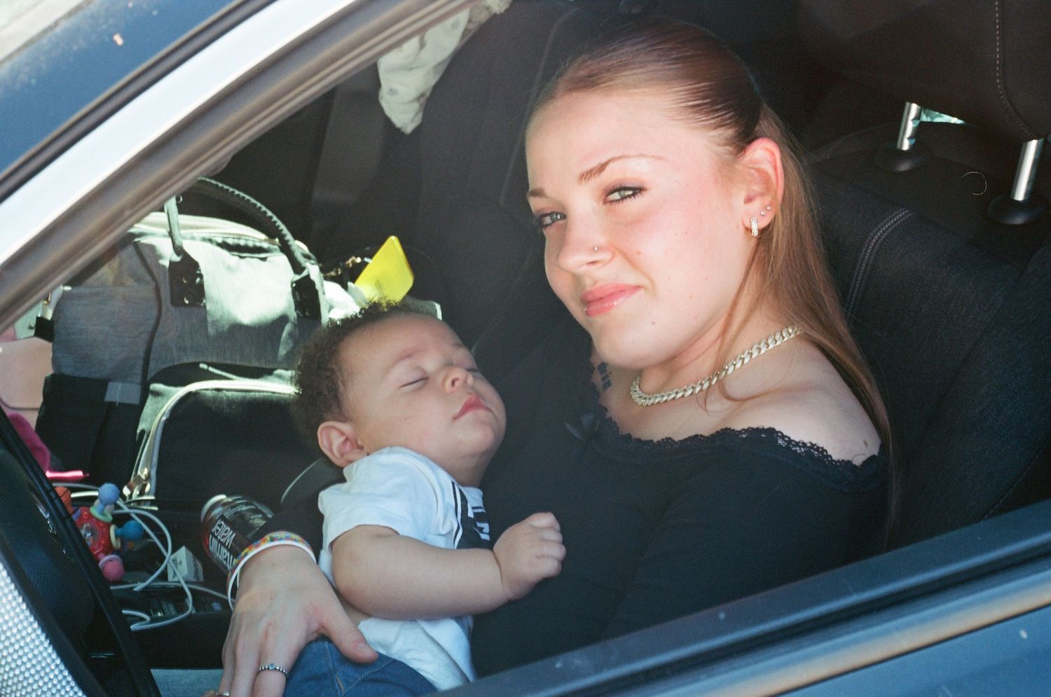 Young mother holding a sleeping newborn baby while sitting inside a car.