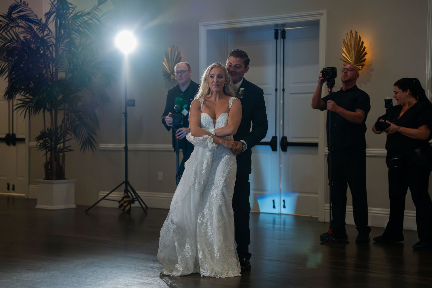 Bride and groom share first dance at elegant wedding reception with photographers nearby.