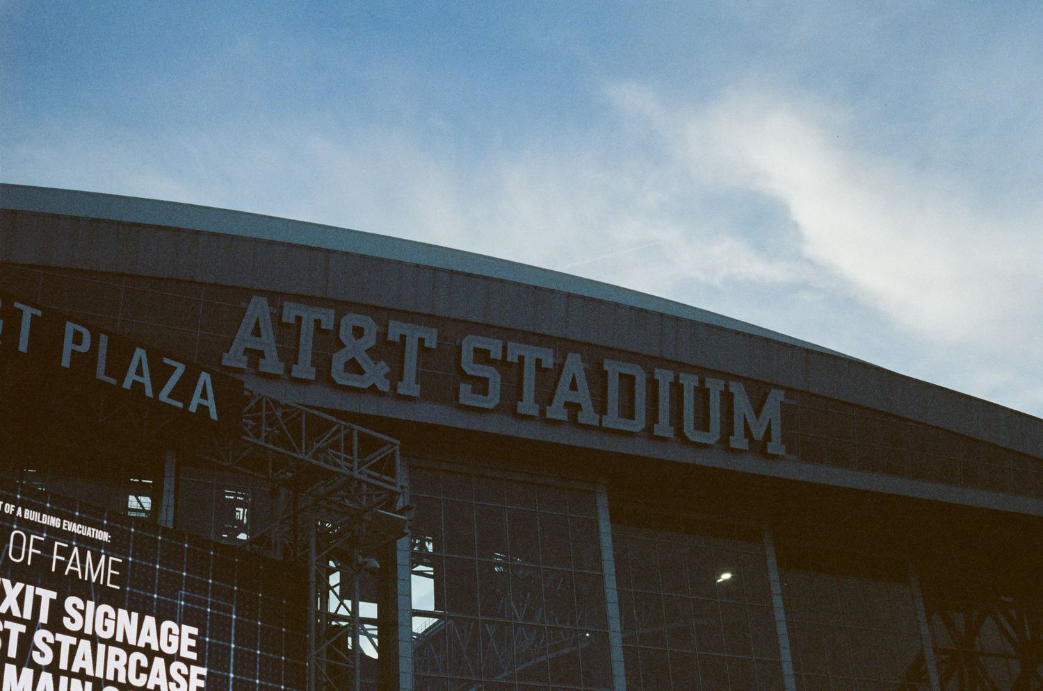 Exterior sign of AT&T Stadium in Arlington, Texas against a partly cloudy sky.