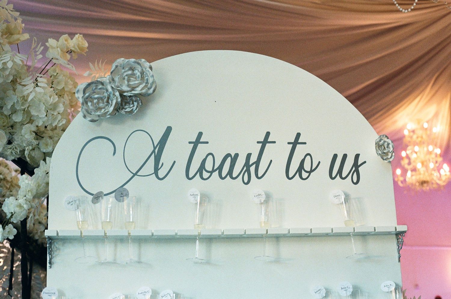 Elegant wedding champagne wall sign reading A Toast To Us decorated with white roses.