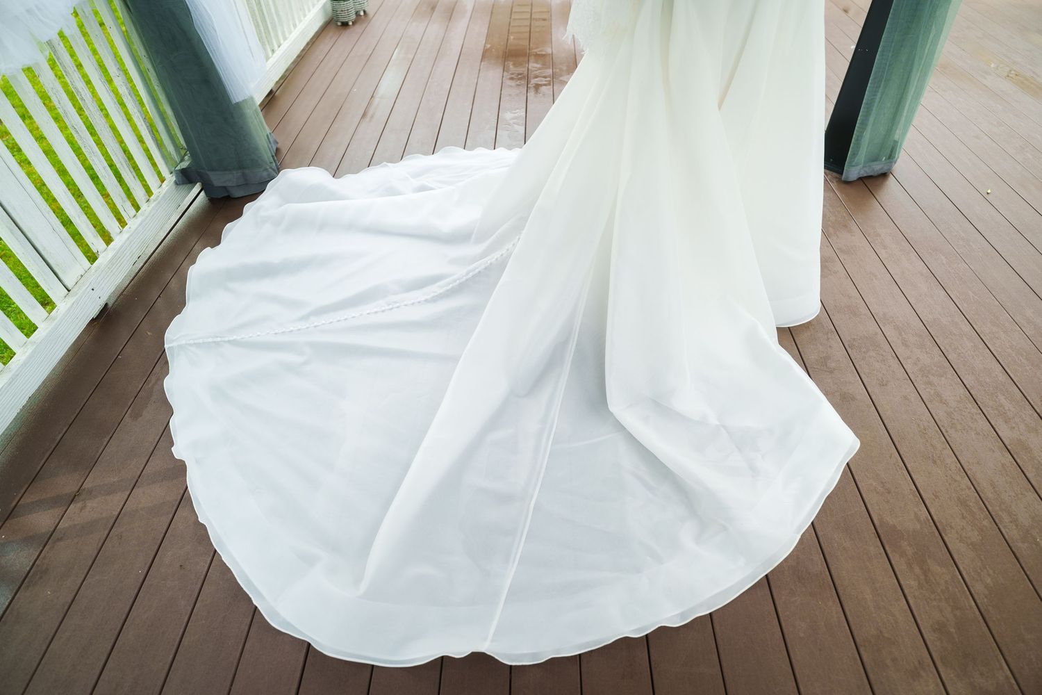 Close-up of flowing white wedding dress train spread across a wooden deck outdoor venue.