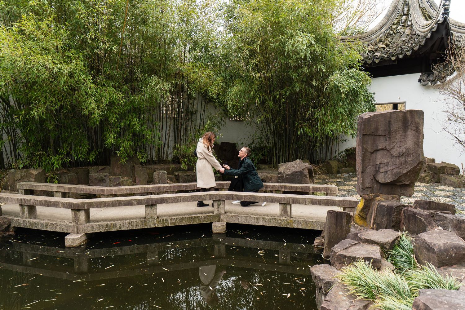 Couple sharing a romantic moment on a stone bridge over a pond in a lush bamboo garden.