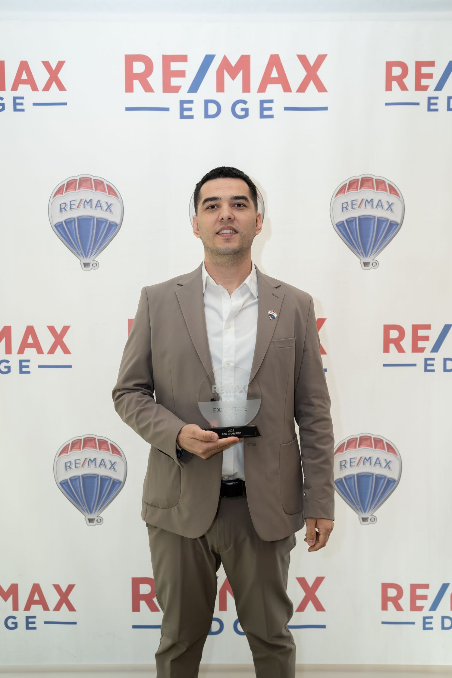 Man in beige suit holds trophy at RE/MAX Edge awards event.