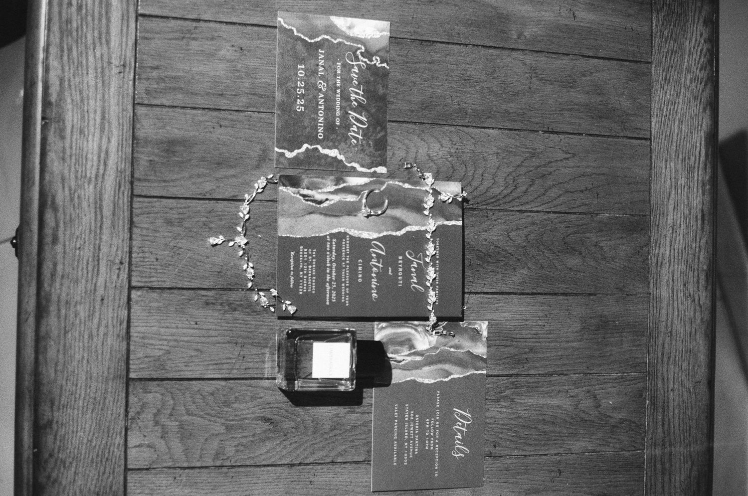 Black and white flat lay of elegant wedding invitation suite with floral details on rustic wood surface.