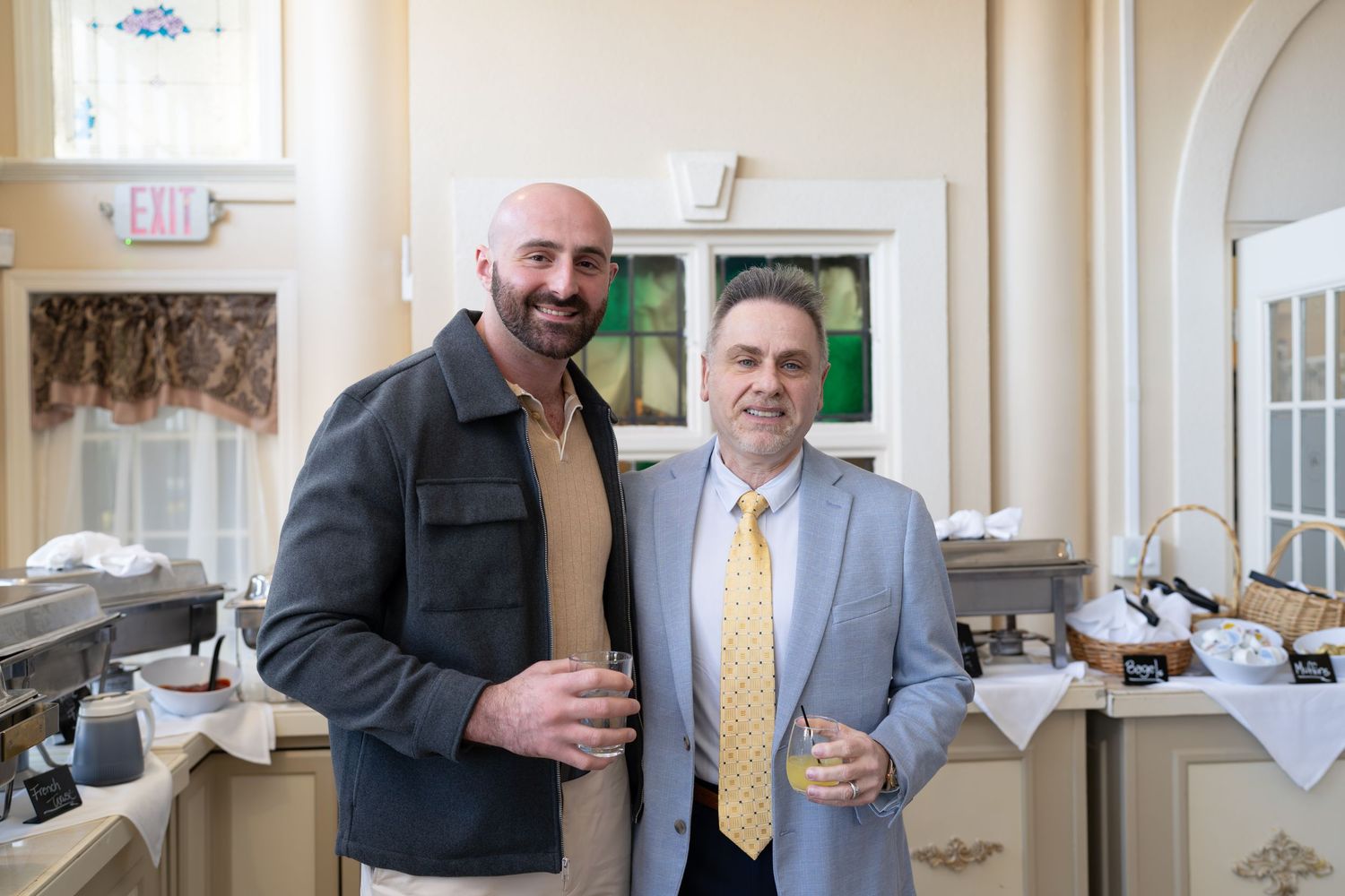 Two men in business attire holding drinks at a RE/MAX Edge real estate gathering.