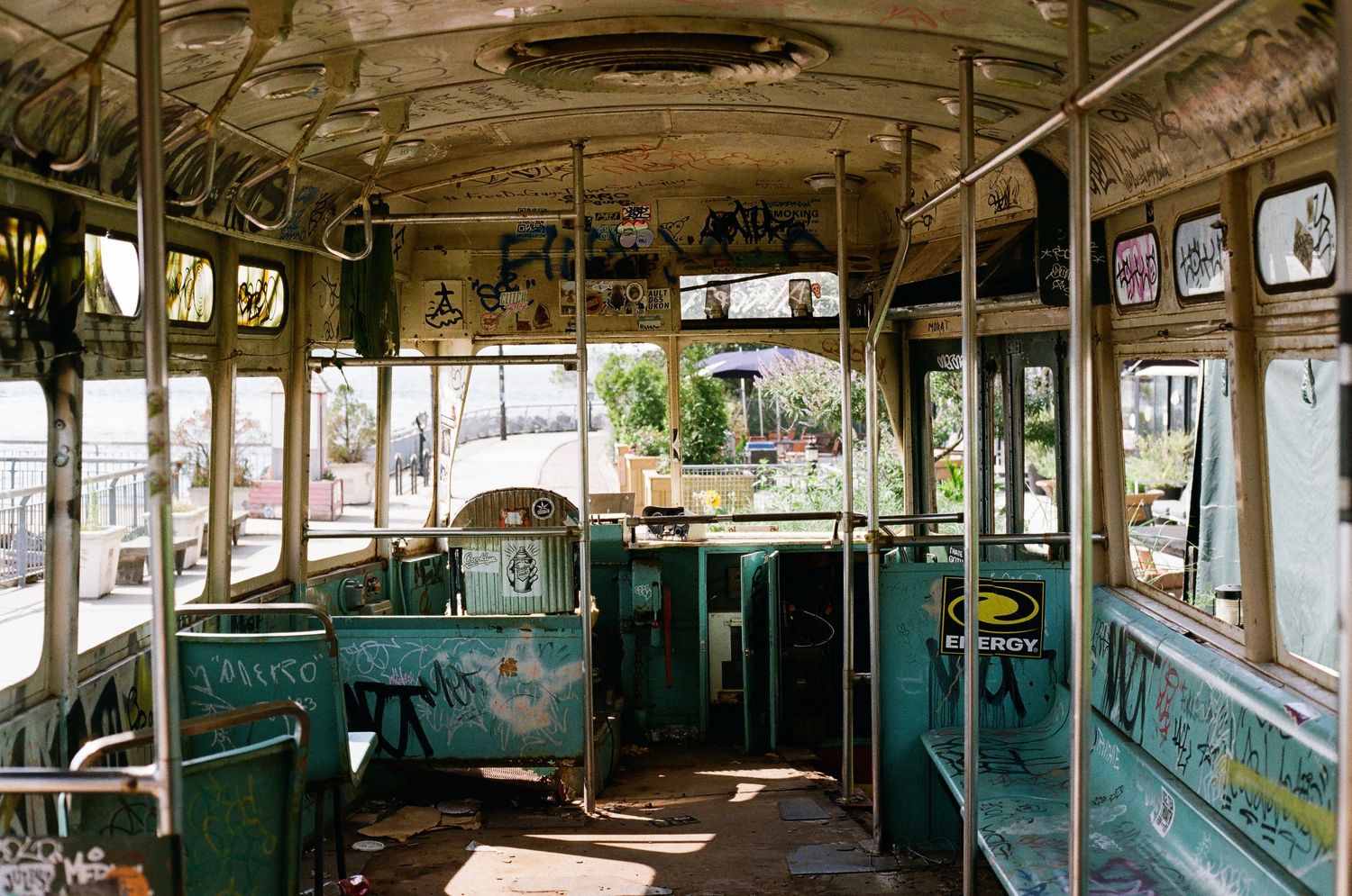 Weathered interior of an abandoned graffiti-covered trolley car with deteriorating green seats and windows.