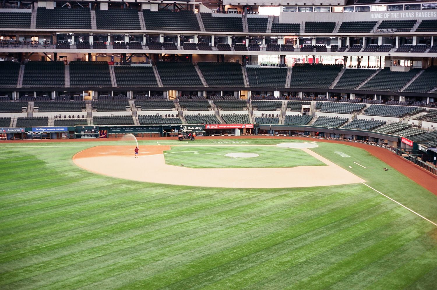 Empty baseball stadium with manicured green field and dirt infield on a clear day.