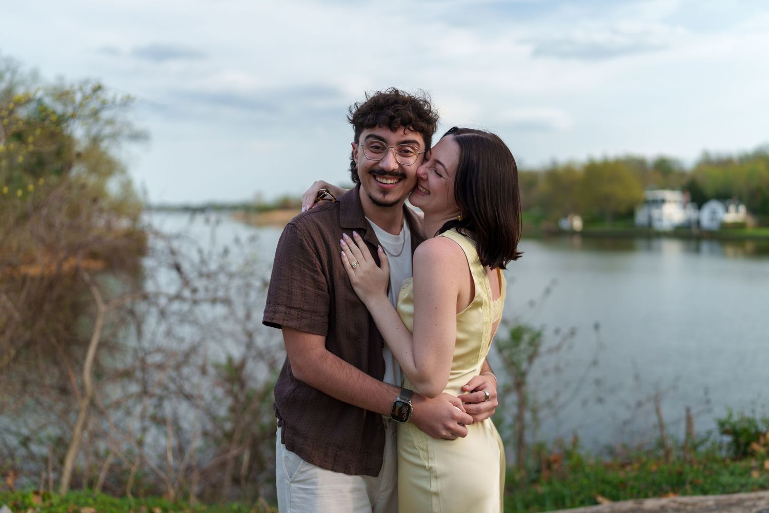 Joyful couple embracing and laughing together near a scenic lakeside on a cloudy day.