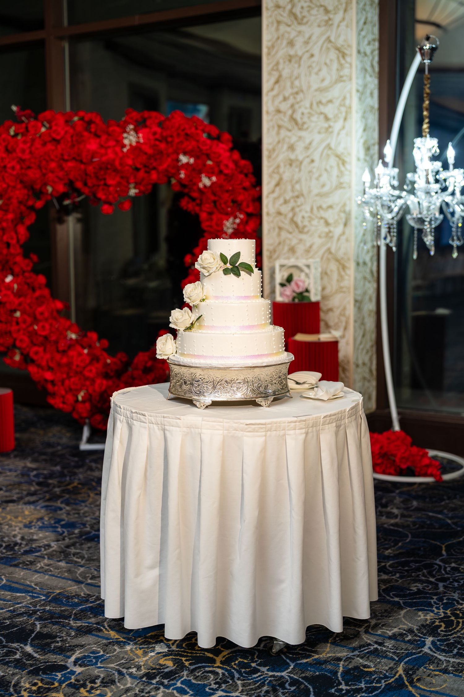 Elegant four-tier white wedding cake decorated with white roses on a silver stand.