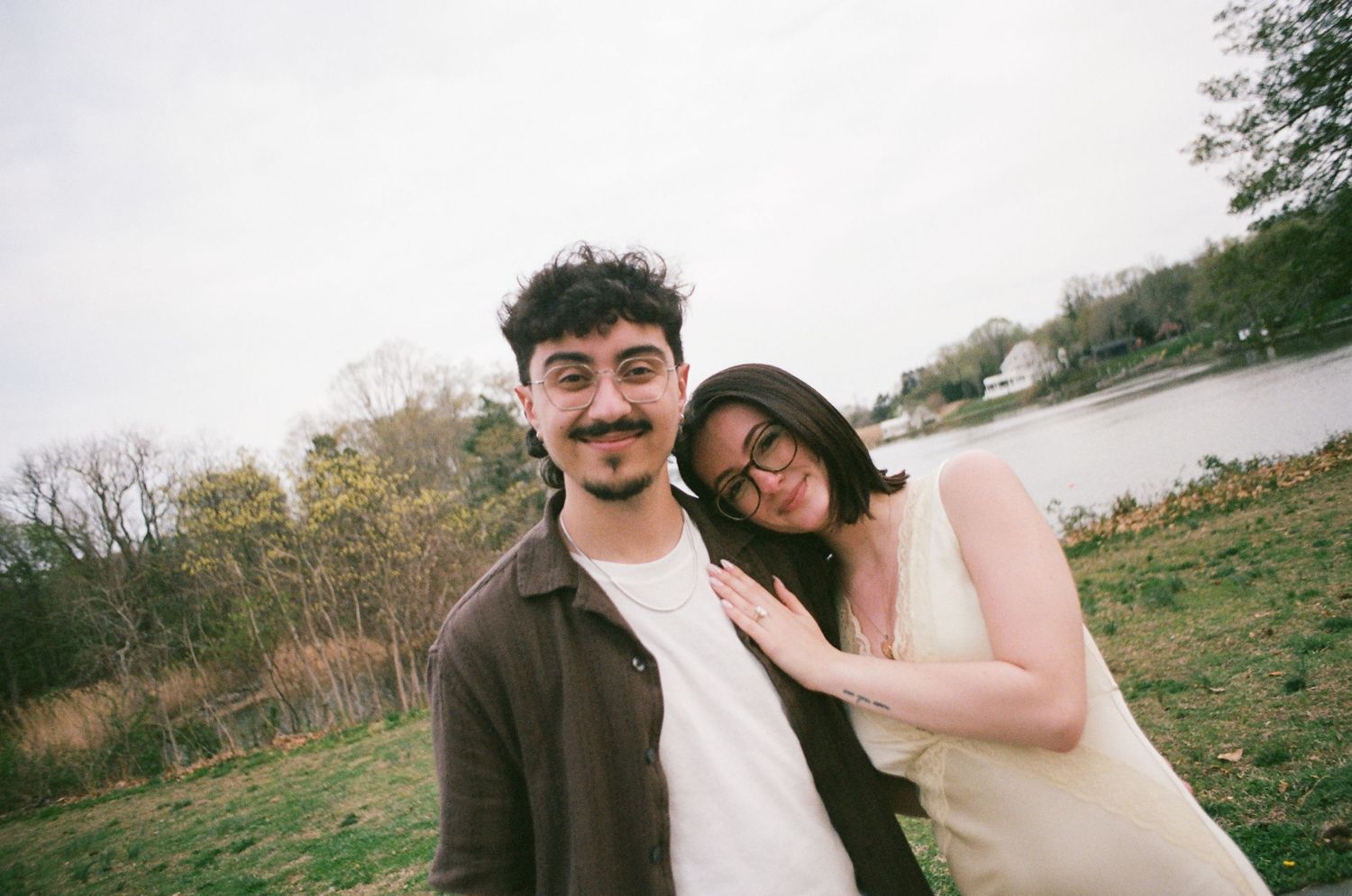 Young couple smiling closely together outdoors near a lake with trees in the background.