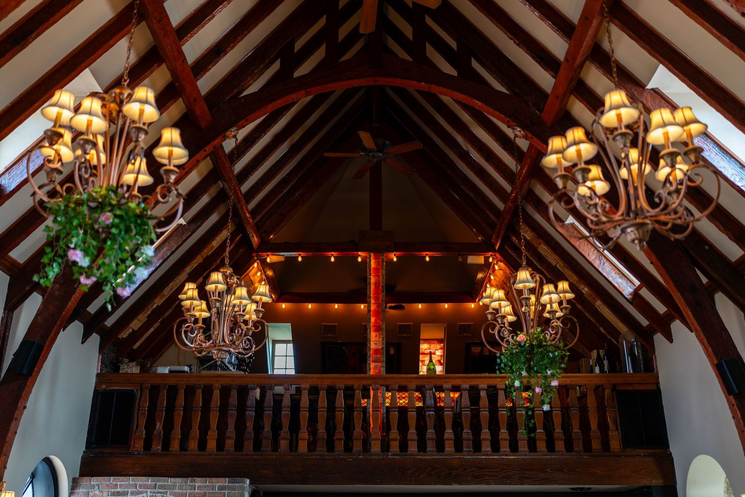 Rustic wooden cathedral ceiling with ornate chandeliers and balcony inside The Stone House venue.