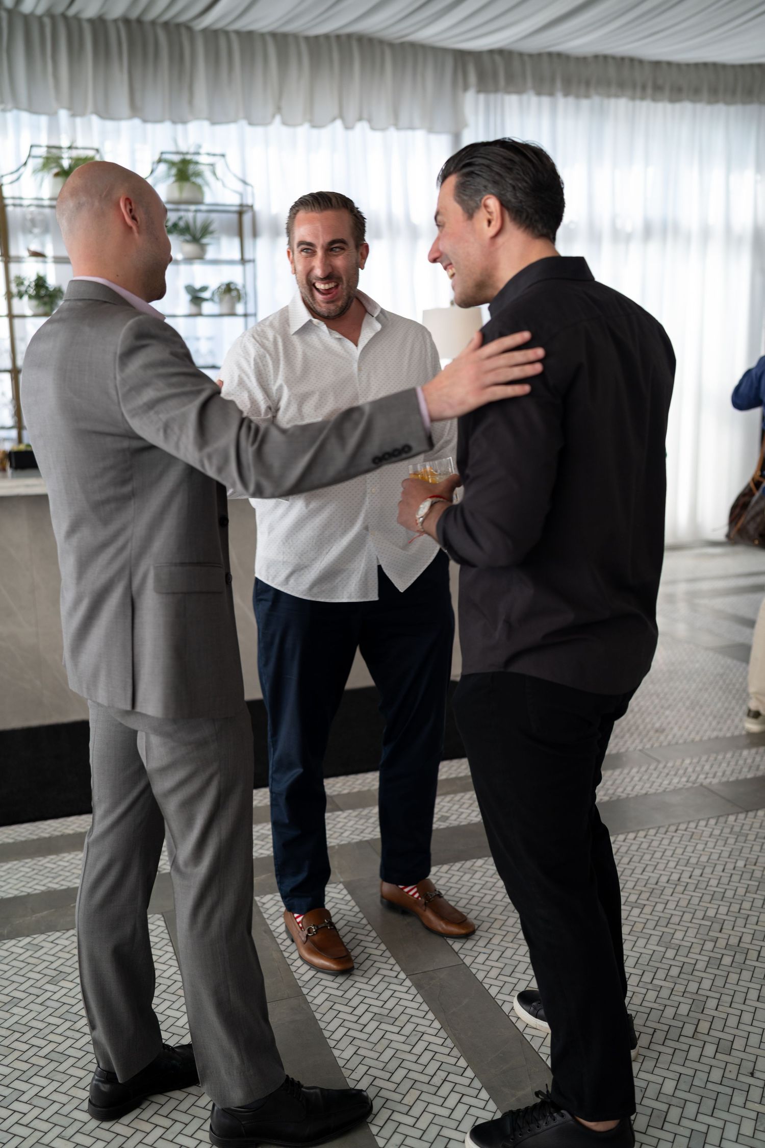 Three men laughing and socializing together inside a bright modern event venue.