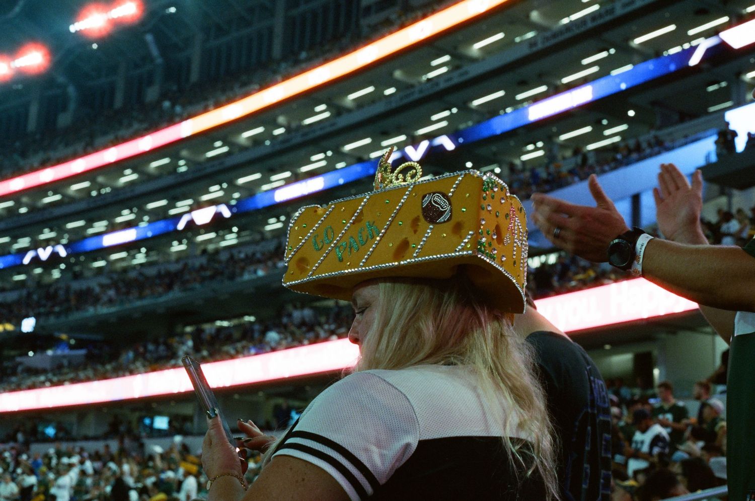 Blonde woman wearing a gold crown at a packed indoor sports arena event.