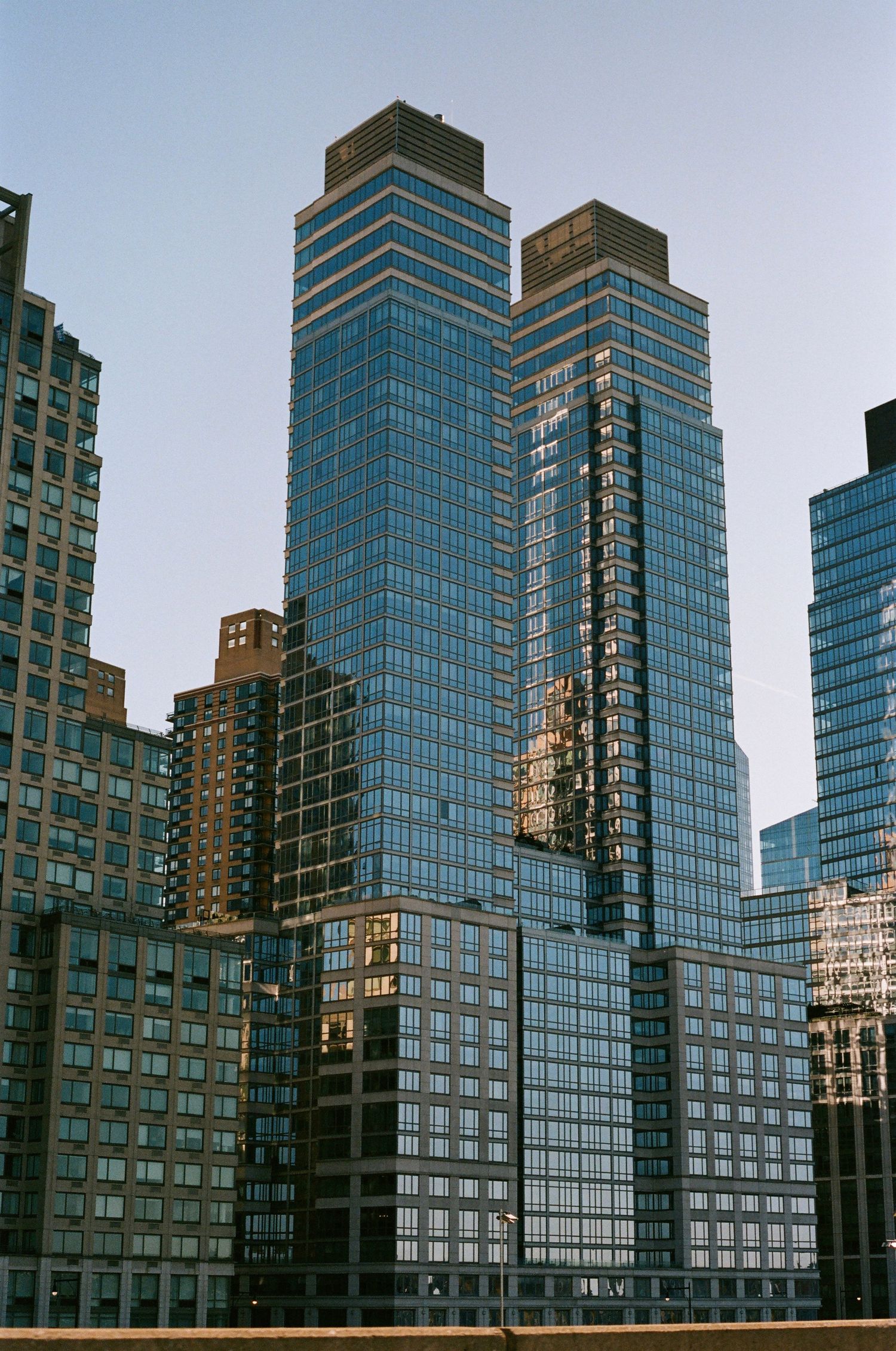 Tall modern glass skyscrapers reflecting sunlight in a dense urban Manhattan cityscape at dusk.