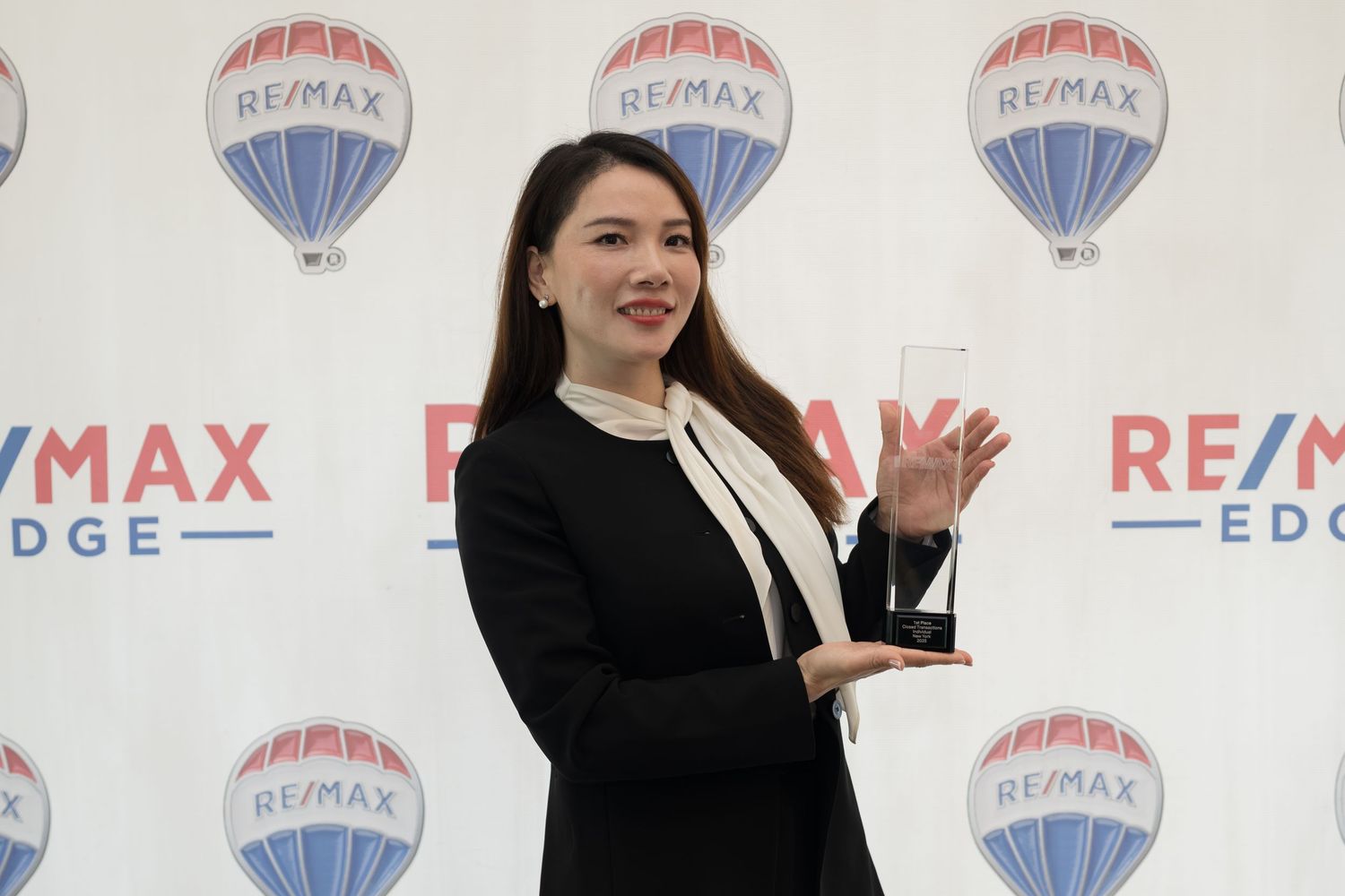 Professional woman in black blazer proudly displays crystal award at RE/MAX Edge ceremony.