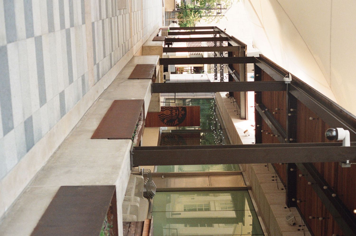 Modern building corridor with glass railings, wooden beams, and tiled walls in perspective view.