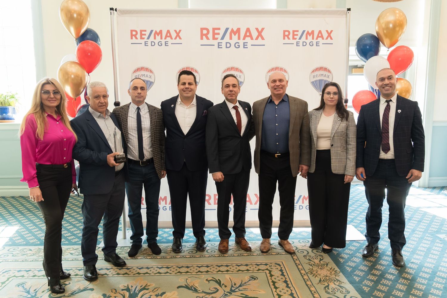 Group of eight RE/MAX Edge real estate professionals posing in front of branded signage with balloons.