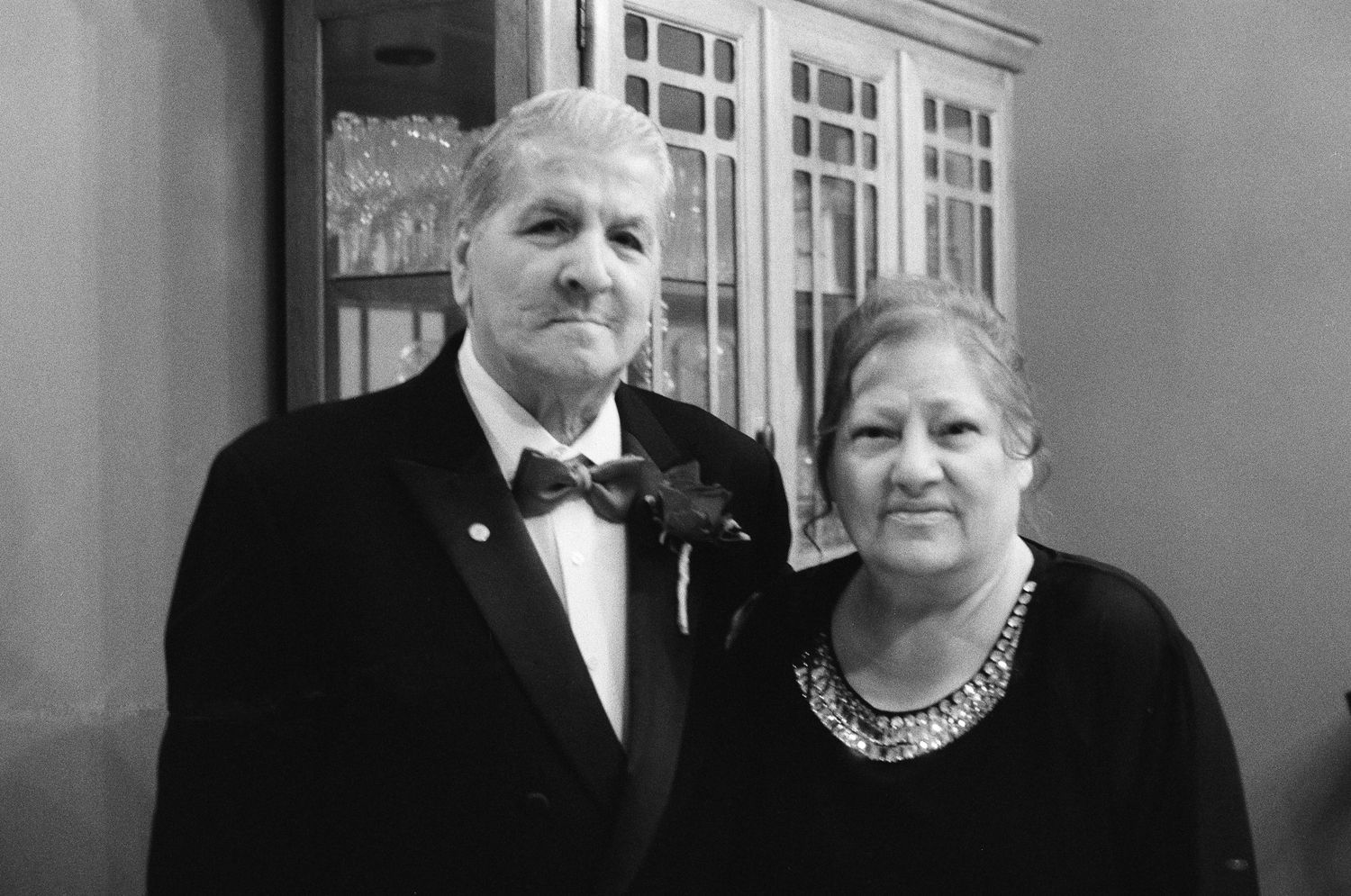 Elegant black and white portrait of an older couple dressed formally, man in tuxedo with boutonniere, woman in black dress.