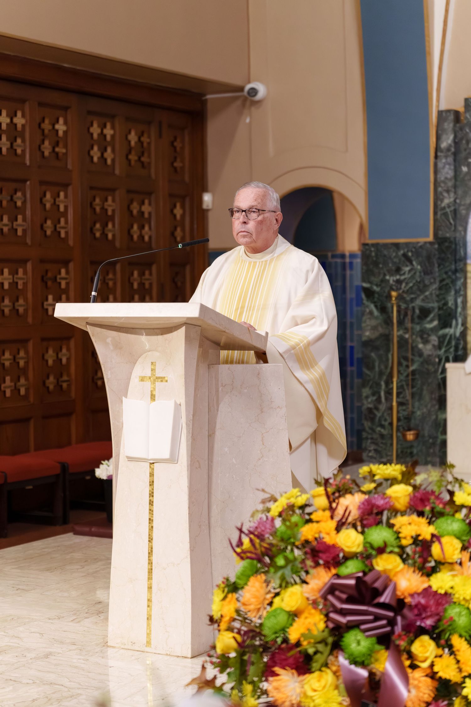 Catholic priest in white and gold vestments delivering a sermon at a church pulpit.