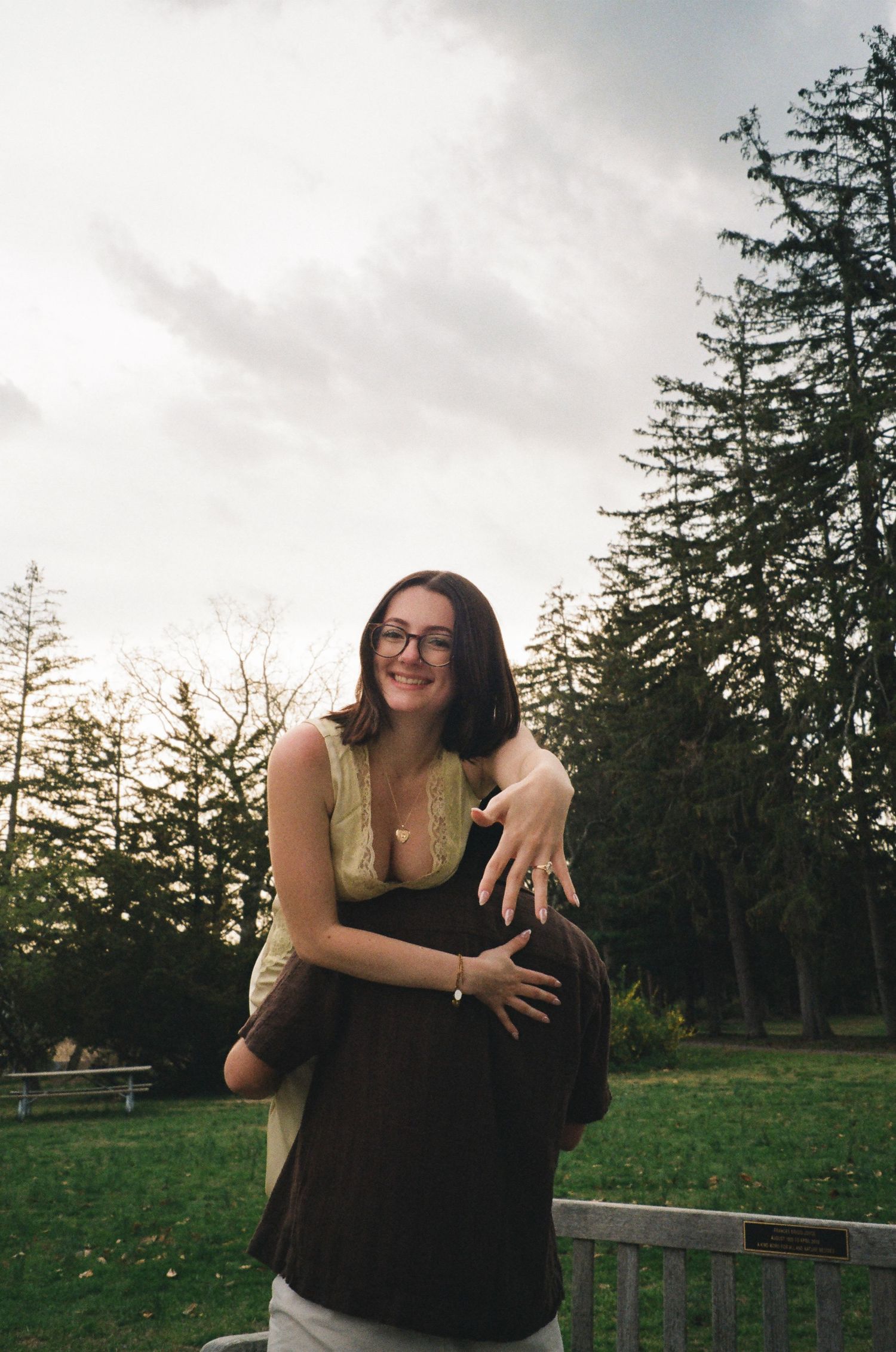 Joyful woman with glasses embracing her partner outdoors in a scenic green park.
