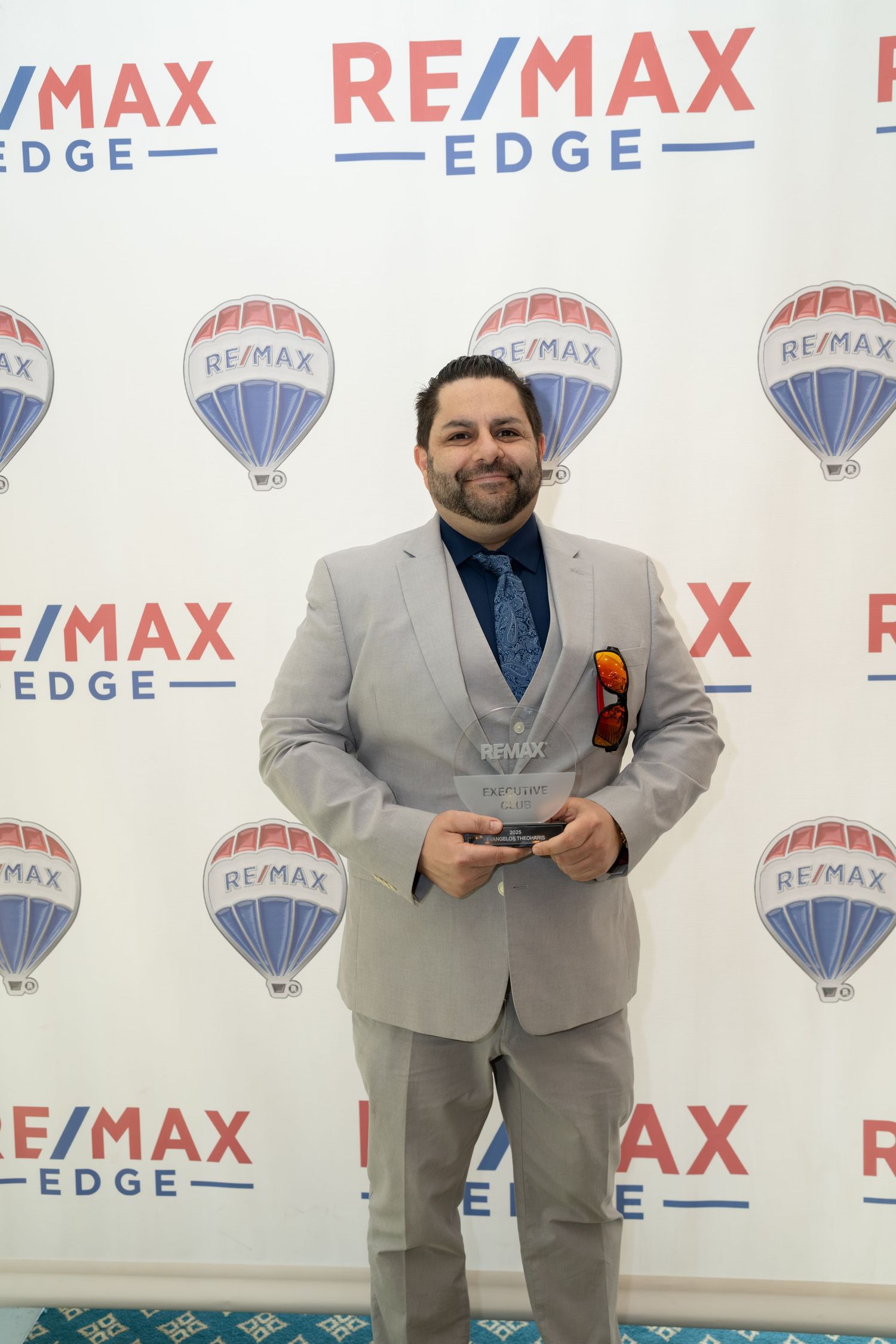 Man in gray suit holds award at RE/MAX Edge awards backdrop.