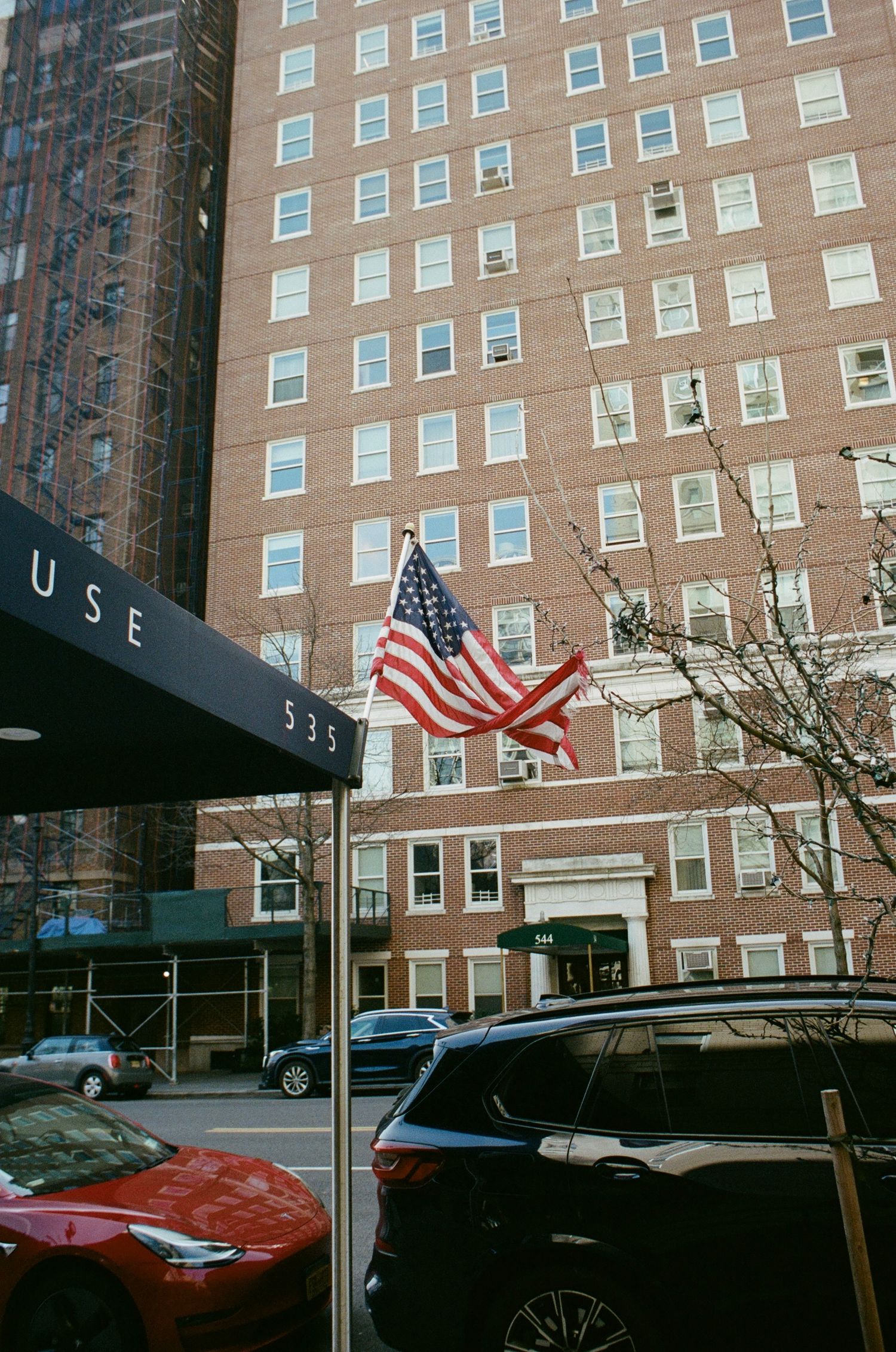 An American flag flies on a pole outside a large brick apartment building numbered 535 in New York City.