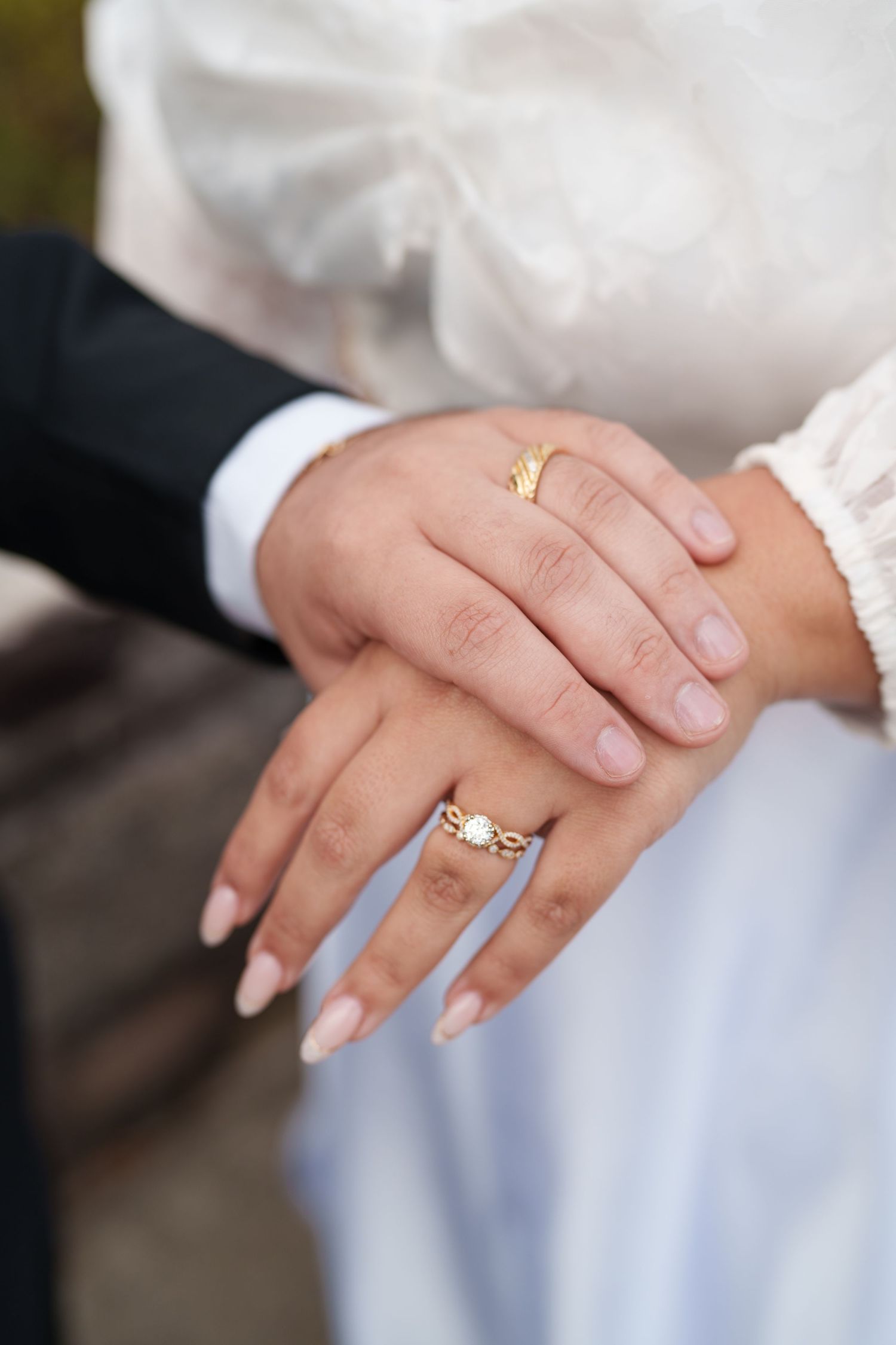 Close-up of bride and groom hands showing gold wedding bands and diamond engagement ring.