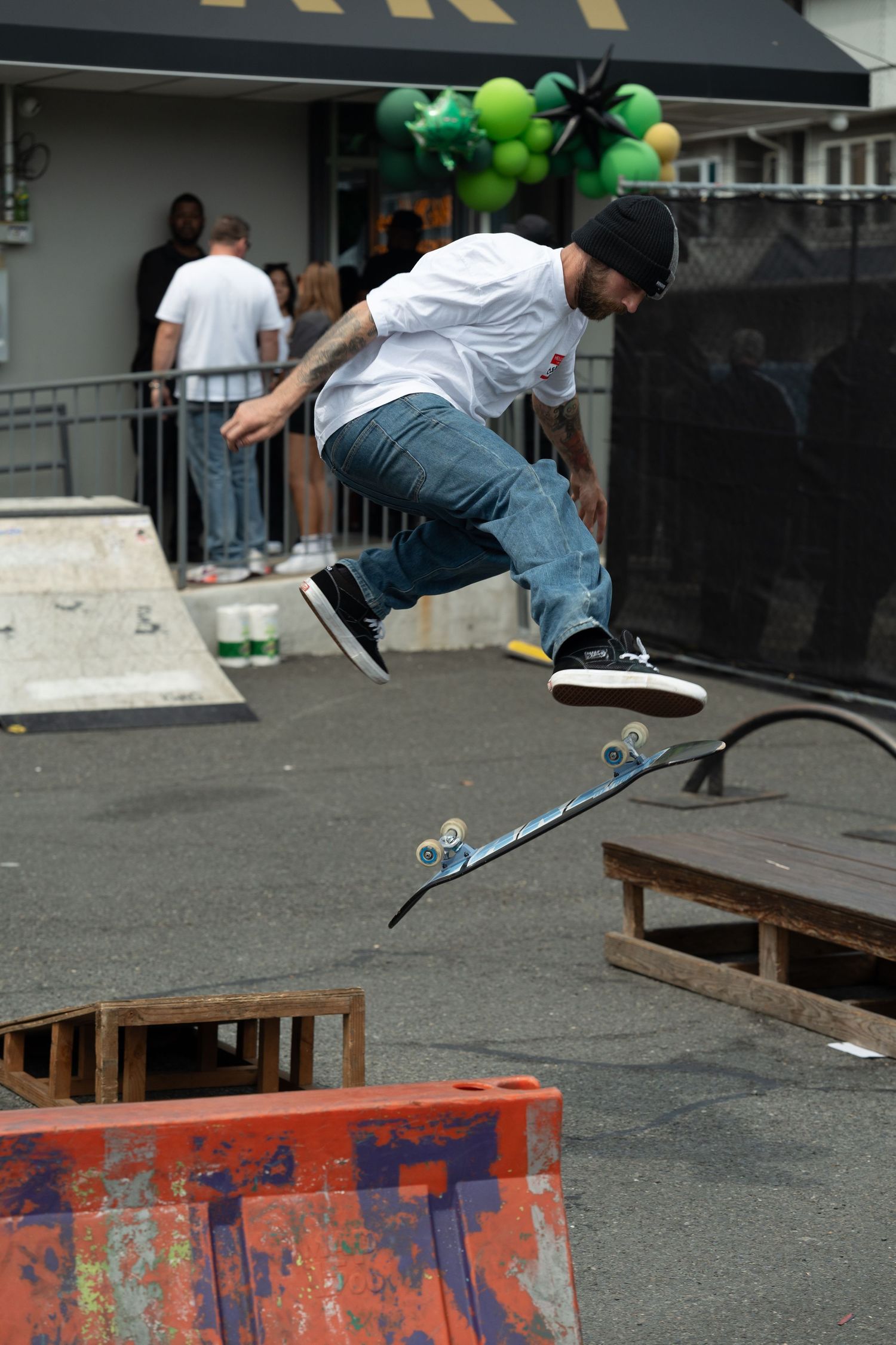 Skateboarder performing a kickflip trick at an outdoor skate park during a dispensary grand opening event.