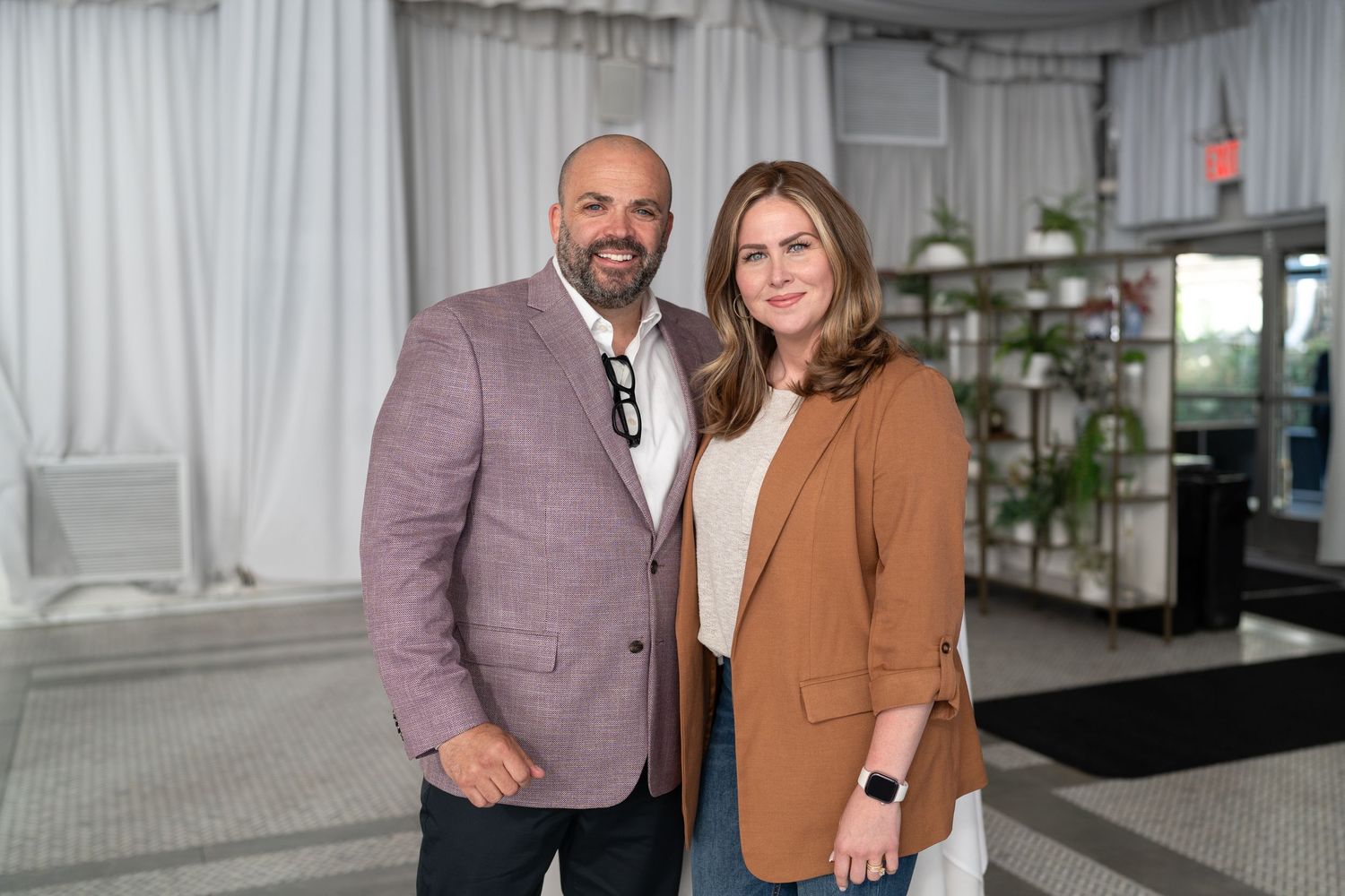 Smiling couple posing together in blazers at an elegant tented venue event.