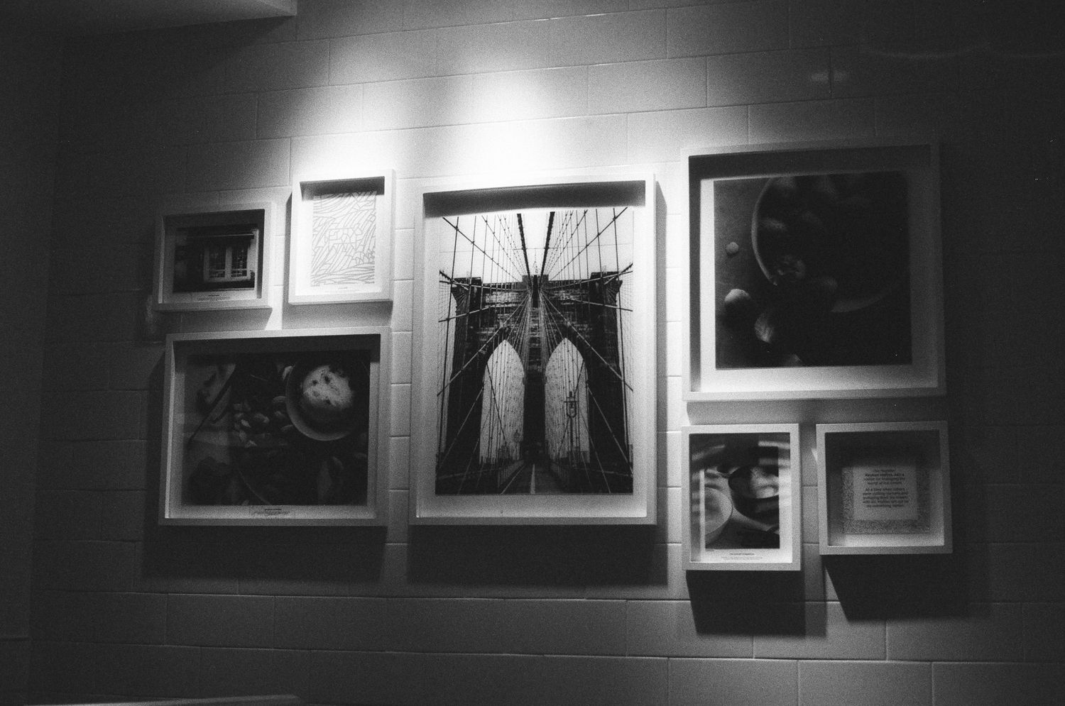 Black and white photo of framed artwork gallery wall featuring Brooklyn Bridge photograph.