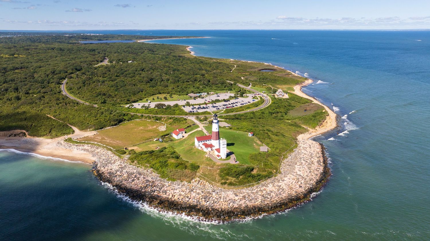 Aerial view of a scenic coastal lighthouse surrounded by rocky shores and lush greenery.