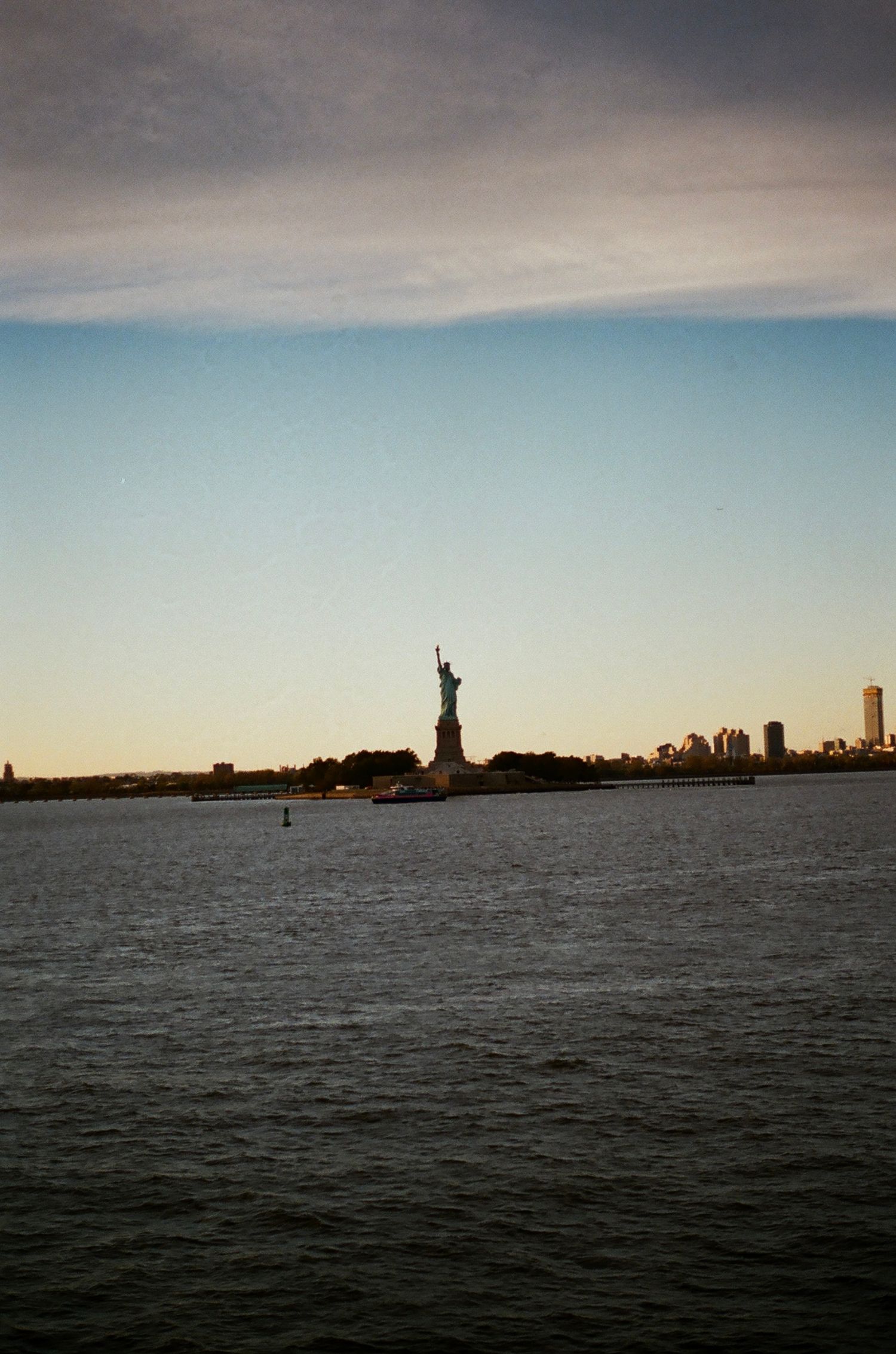 Statue of Liberty silhouetted against a golden sunset sky on New York Harbor.