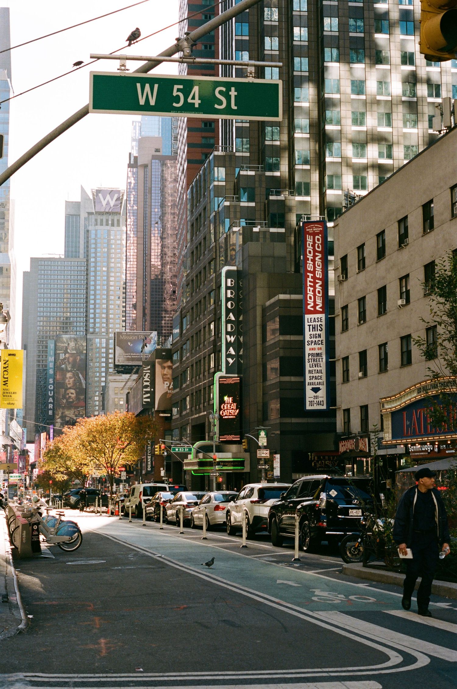 Busy Broadway street view at W 54th St intersection in Midtown Manhattan on a sunny autumn day.