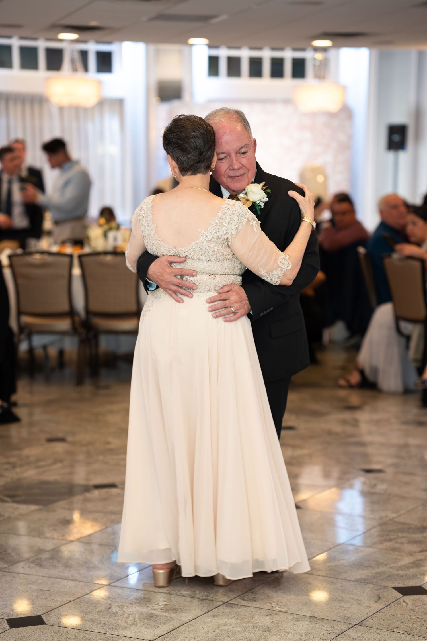 Elegant couple shares romantic anniversary dance in decorated ballroom with seated guests.