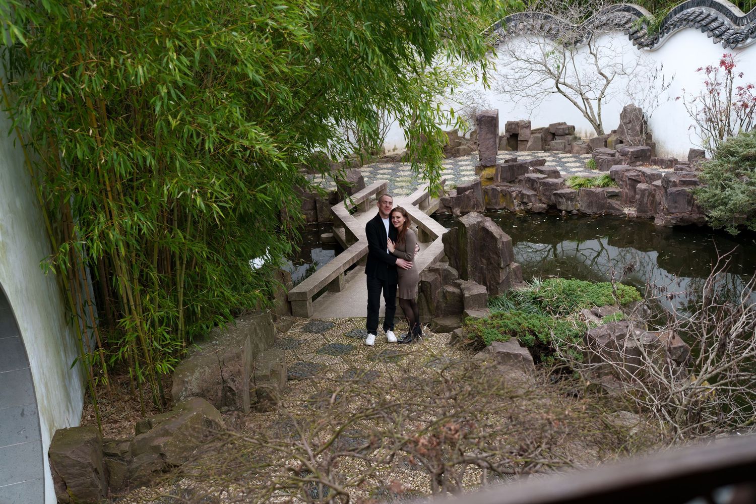 Couple posing together in a traditional Chinese garden with bamboo, rocky landscape, and a serene pond.