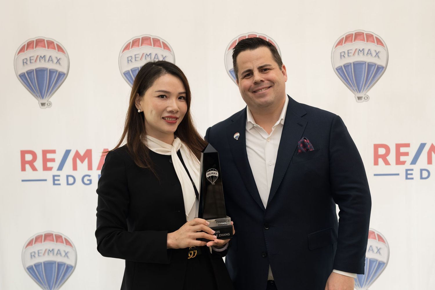 Female RE/MAX Edge agent receives crystal award alongside male colleague at professional ceremony.