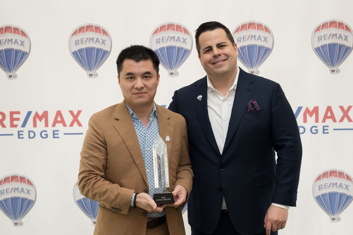 Two RE/MAX Edge real estate agents pose with a crystal award at a RE/MAX Edge recognition event.