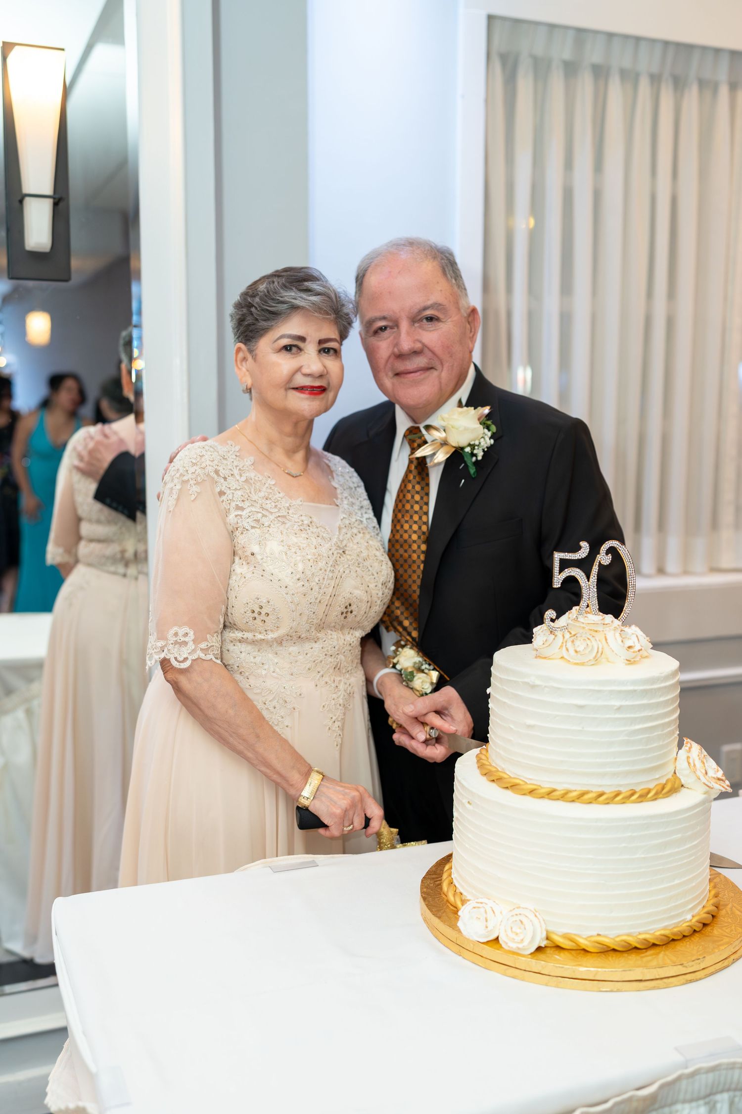 Couple celebrates 50th wedding anniversary cutting tiered white and gold celebration cake.