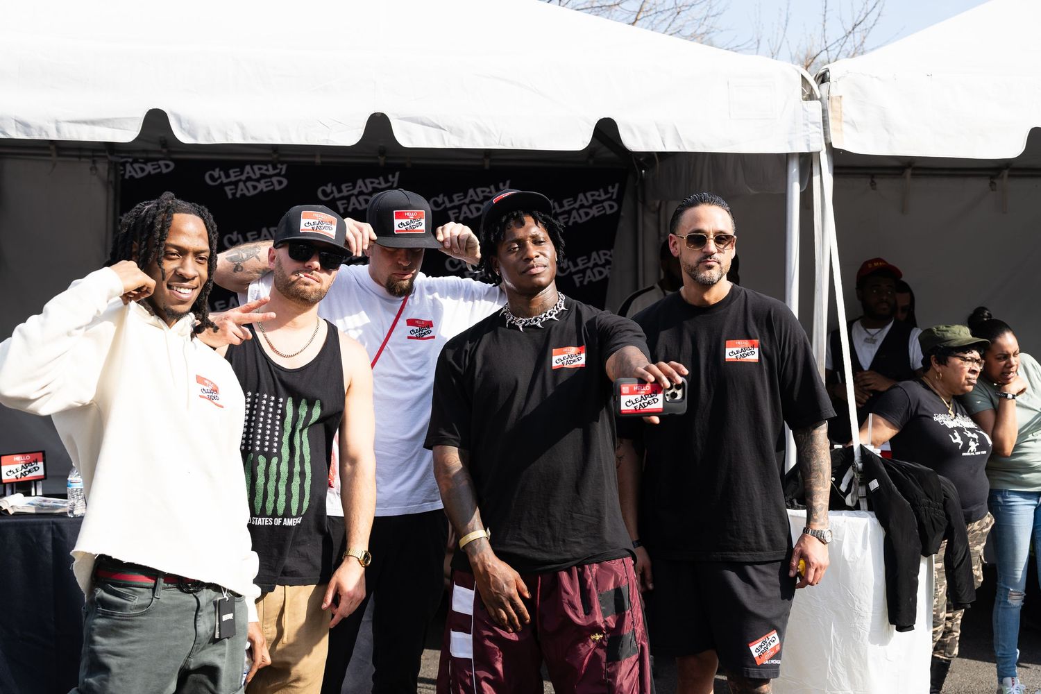 Group of five men posing together under a white event tent at an outdoor hip-hop festival.