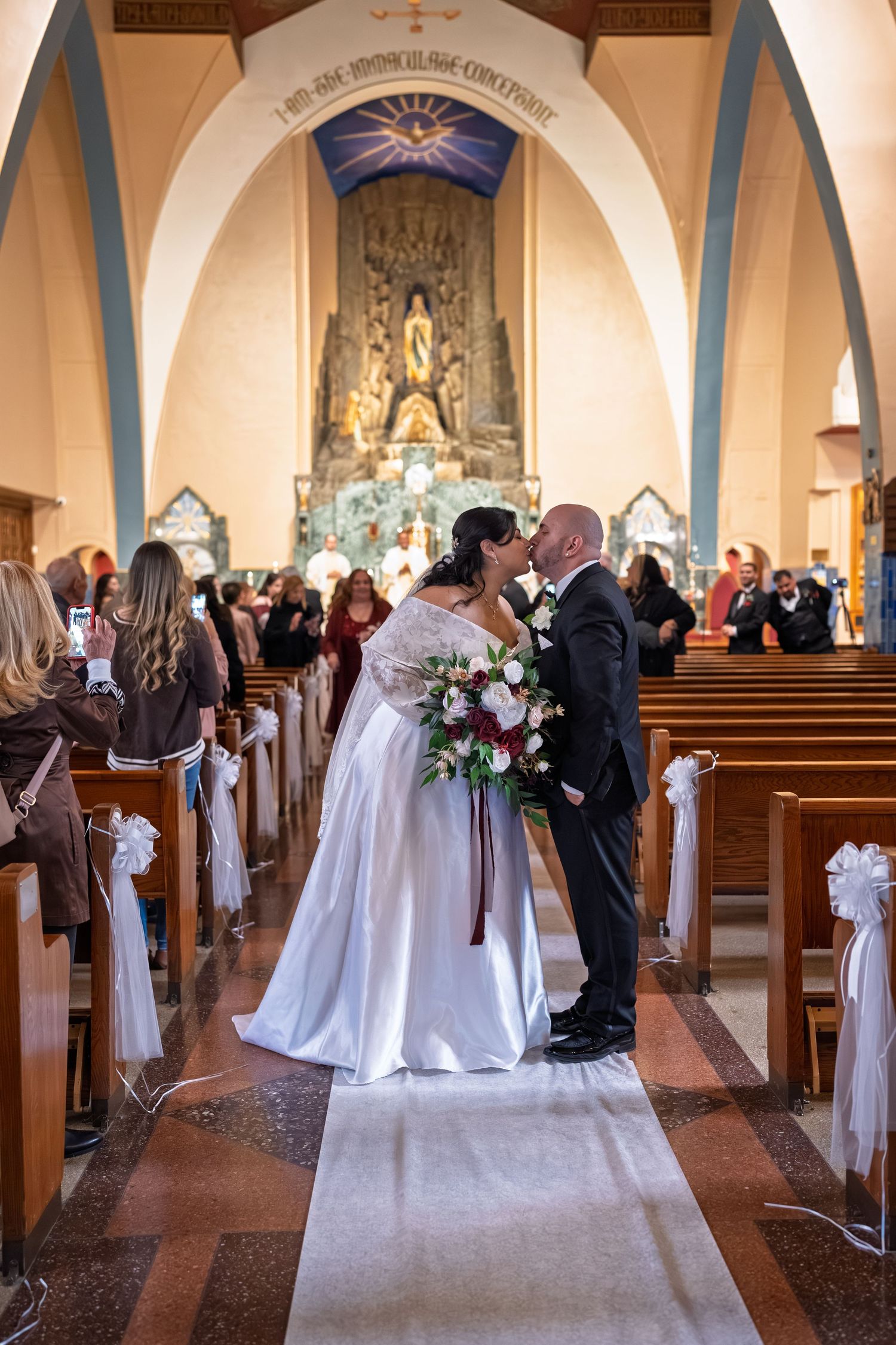 Bride and groom share first kiss at church altar while guests celebrate in the pews.