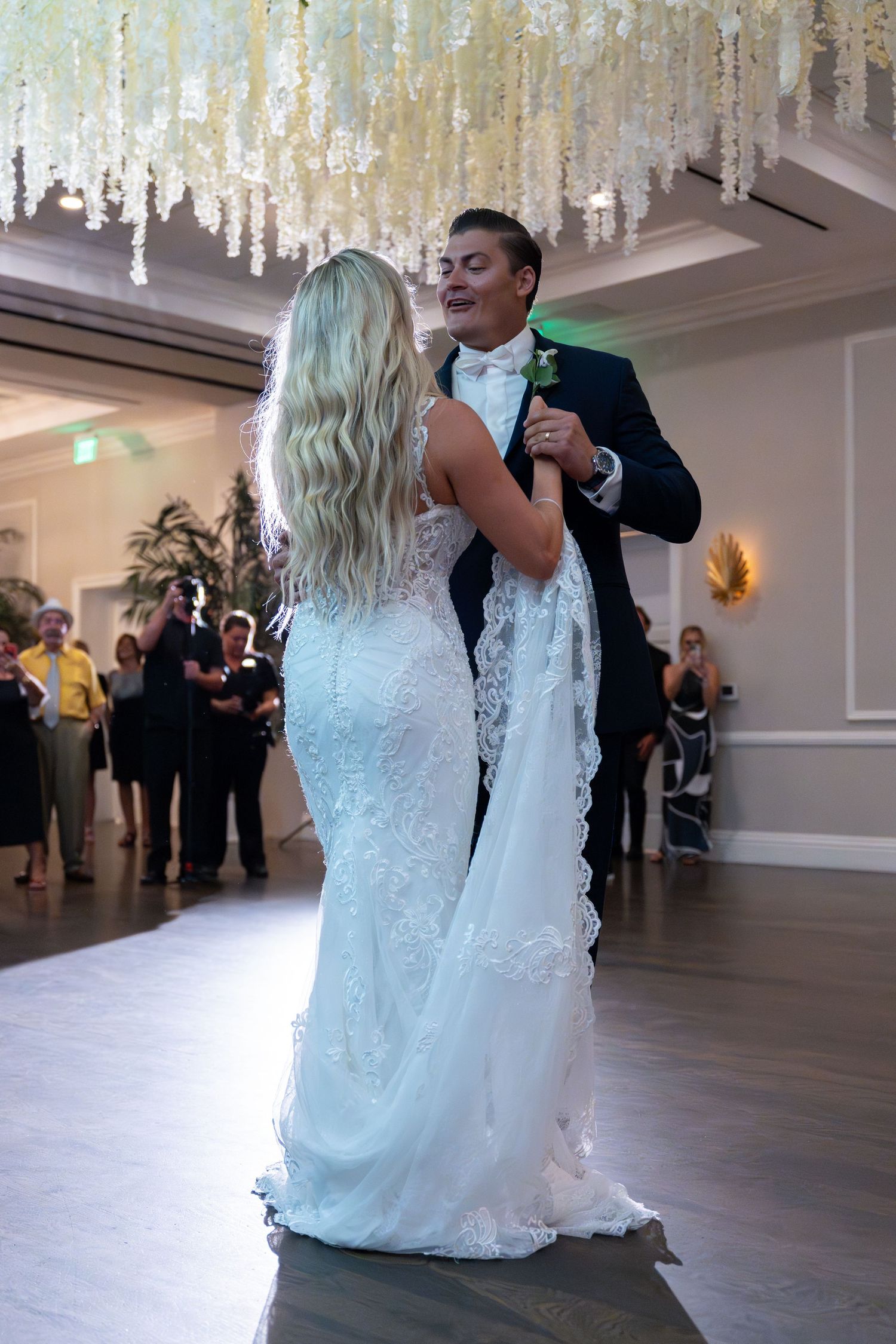 Bride and groom dance together under floral chandelier at elegant wedding reception.