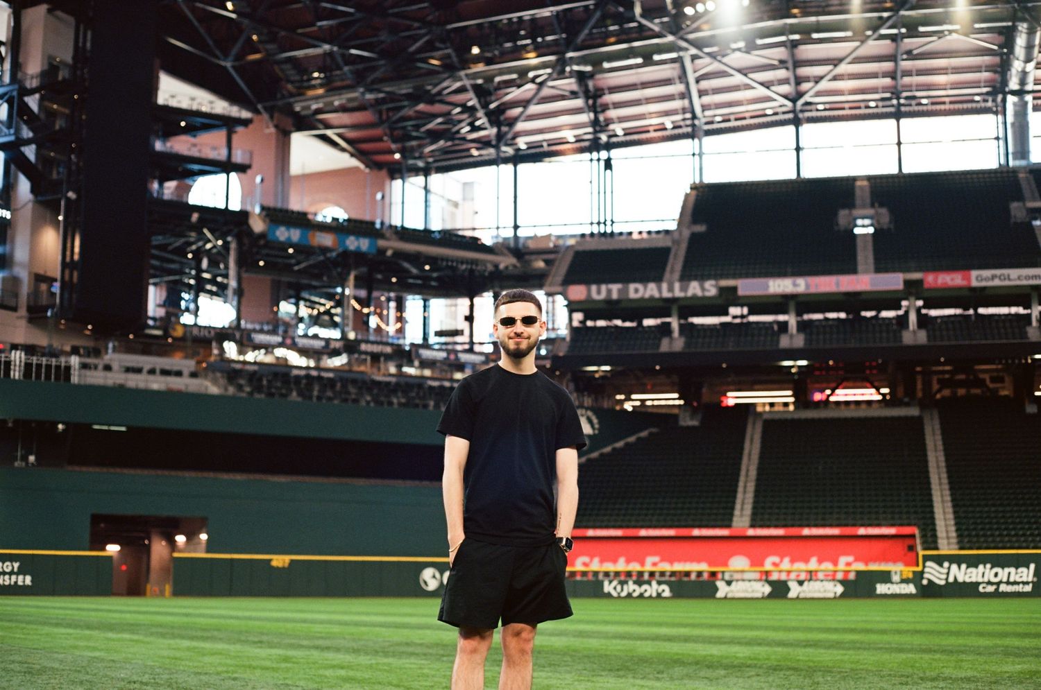 Man in black outfit standing on the field inside a domed baseball stadium with green turf.